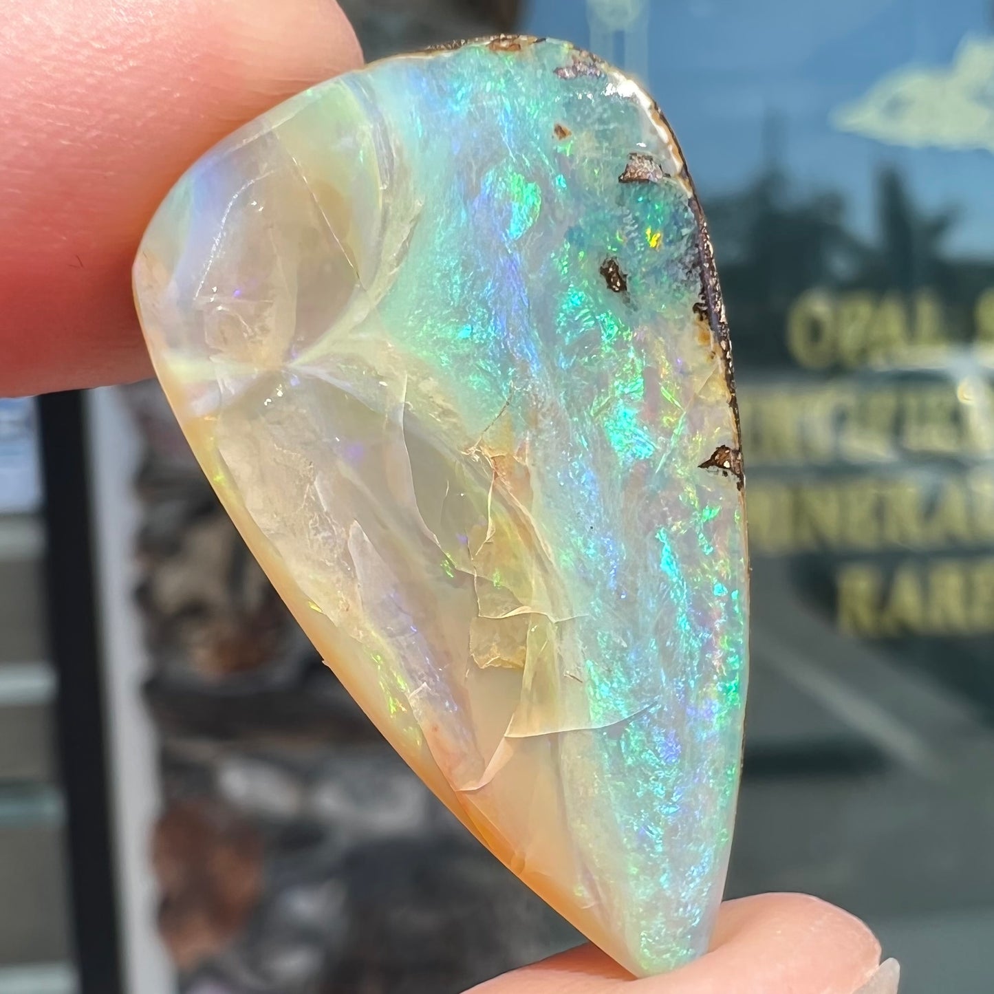 A loose, pear shaped boulder opal stone from Queensland, Australia. Predominant colors are blue, purple, and green.