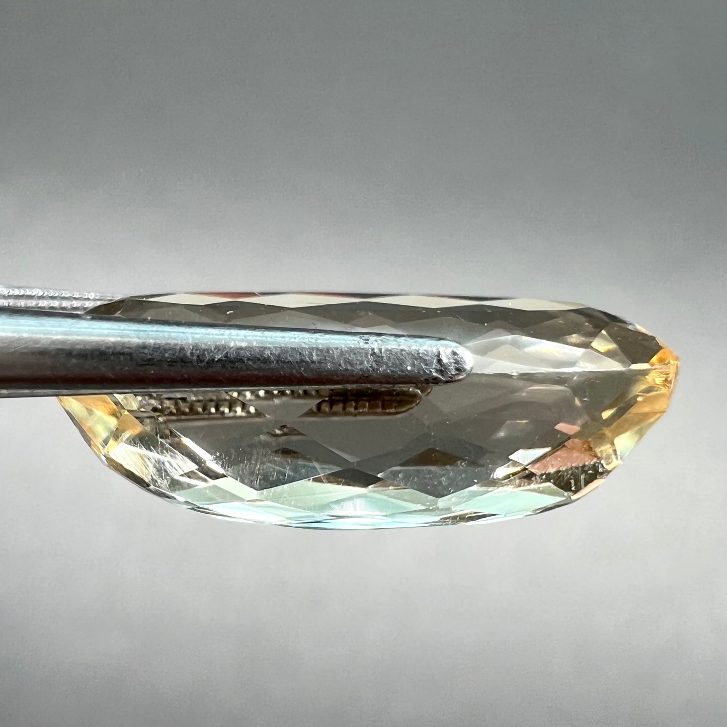 A loose, oval cut golden topaz gemstone. A stronger concentration of yellow rests in the edges of the stone.