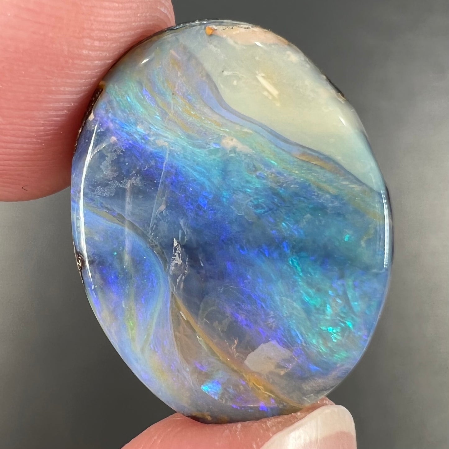 A loose, oval cabochon cut Australian boulder opal stone.