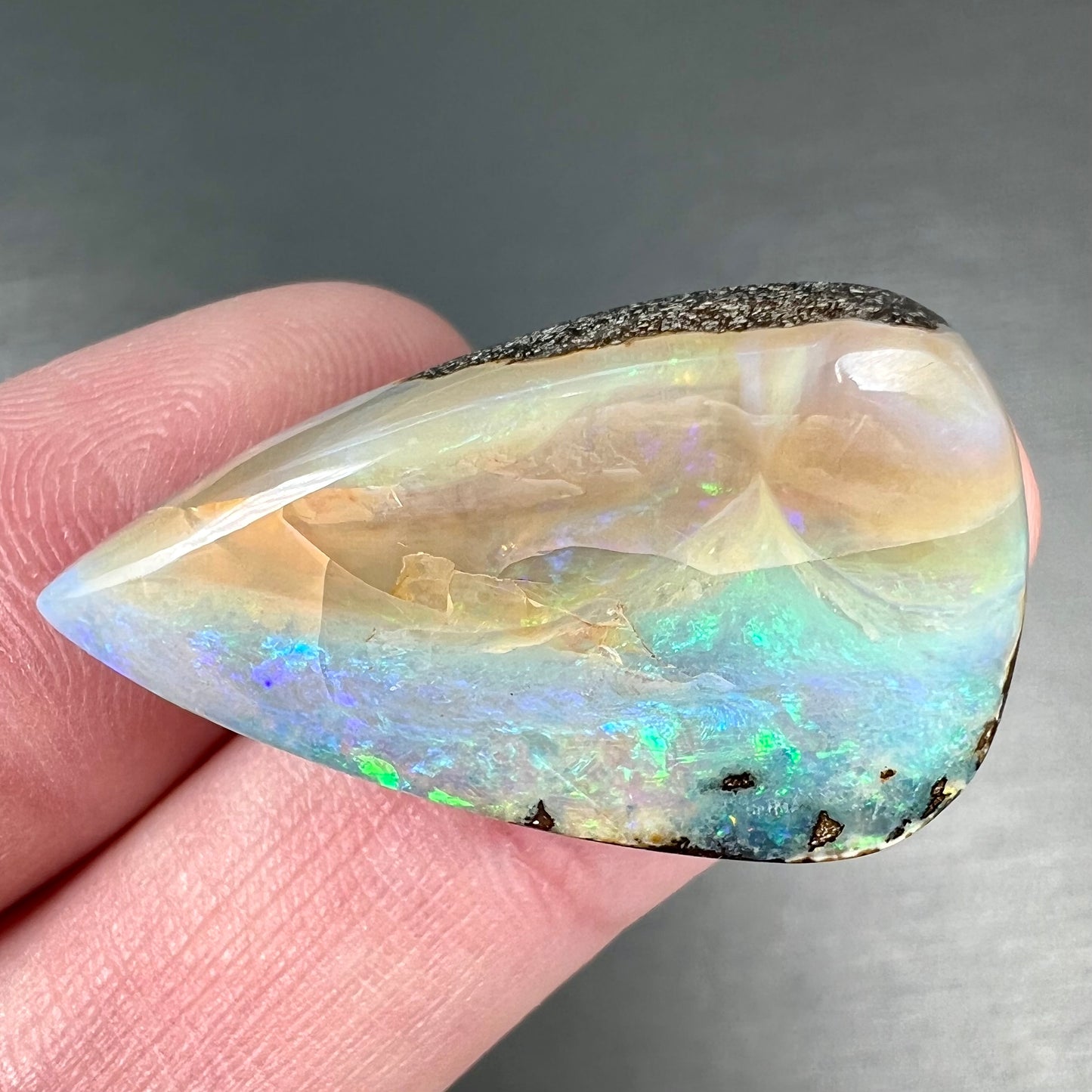 A loose, pear shaped boulder opal stone from Queensland, Australia. Predominant colors are blue, purple, and green.