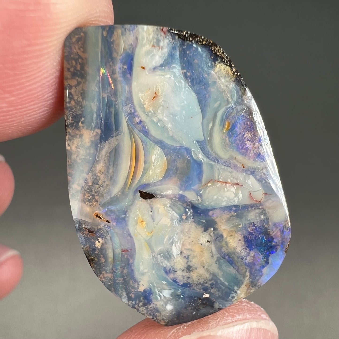 A loose, polished, freeform cut boulder opal stone from Queensland, Australia.