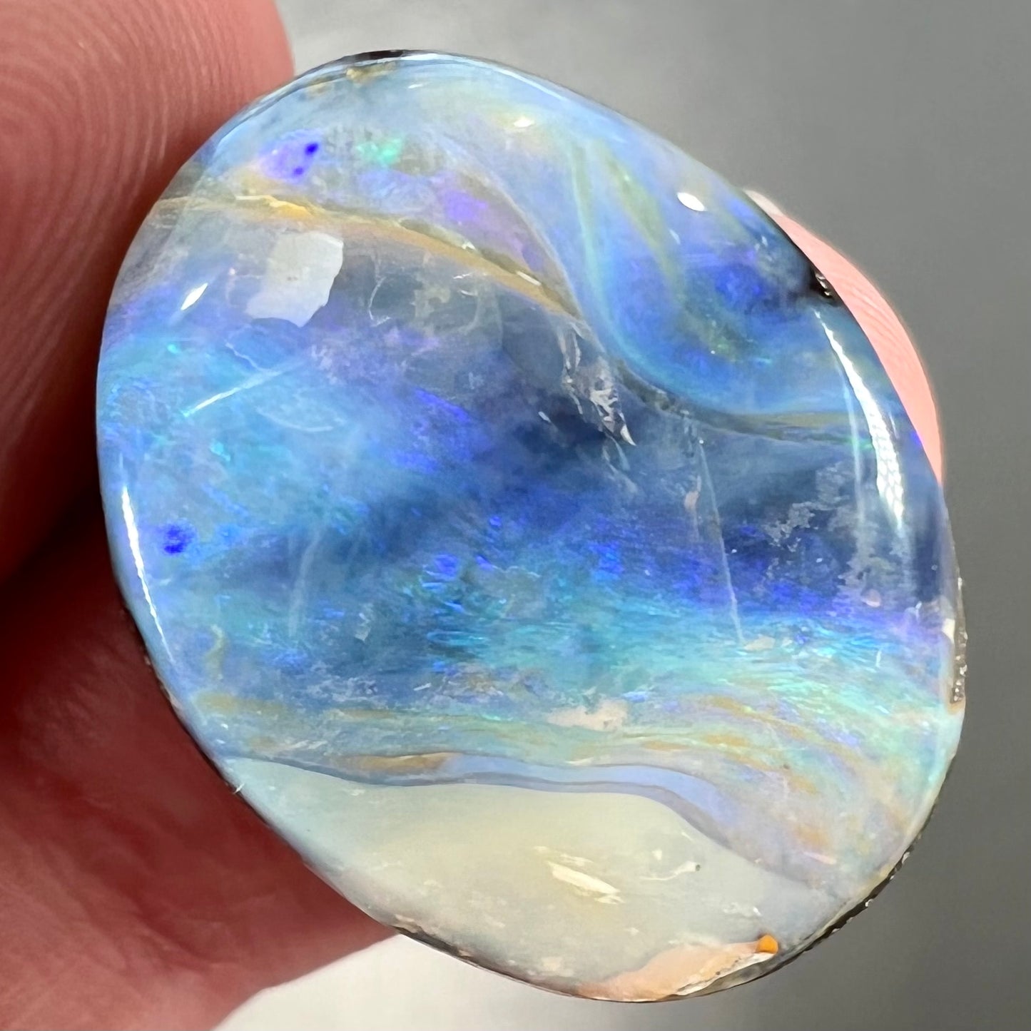 A loose, oval cabochon cut Australian boulder opal stone.