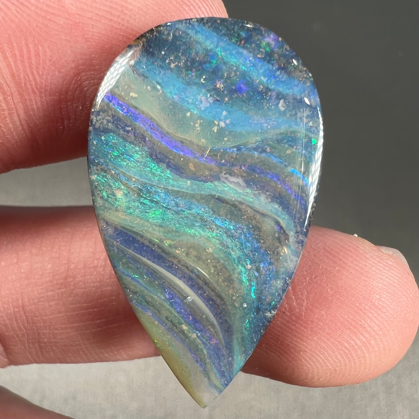 A loose, pear shaped boulder opal stone from Quilpie, Australia. The stone is predominantly blue, green, and purple with red and orange undertones.