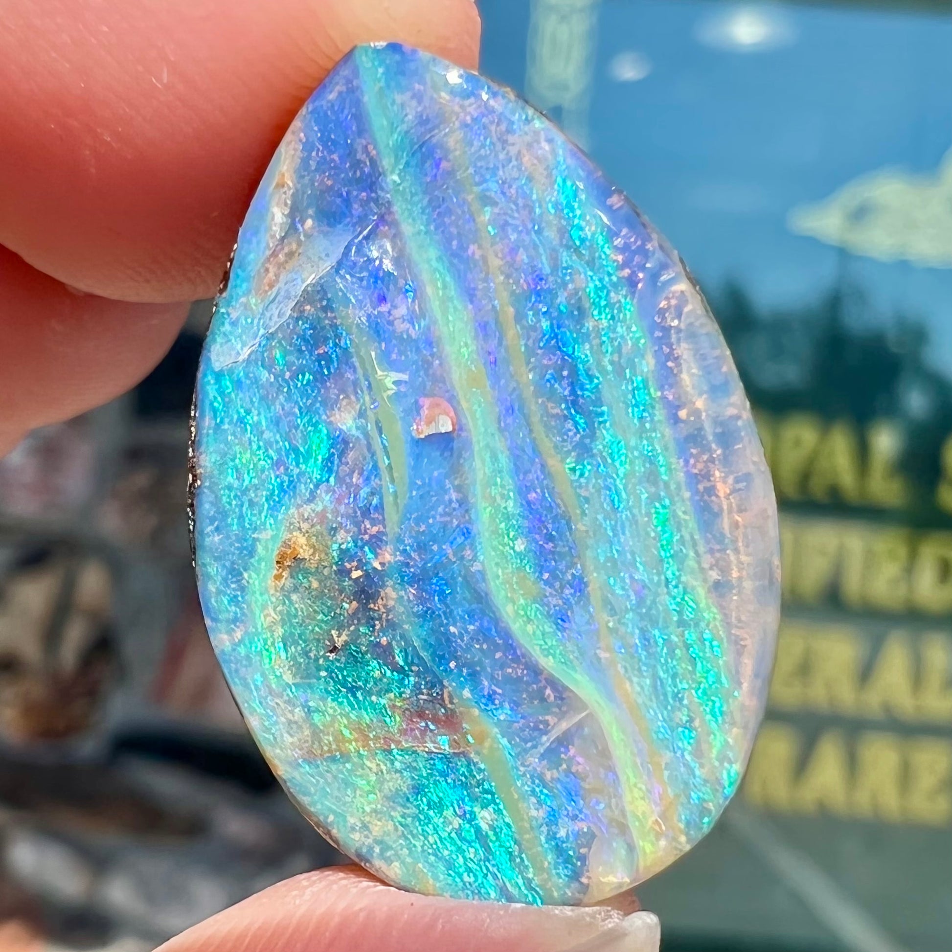 A loose, pear shaped Australian boulder opal stone.  The predominant colors are purple, green, and aqua.