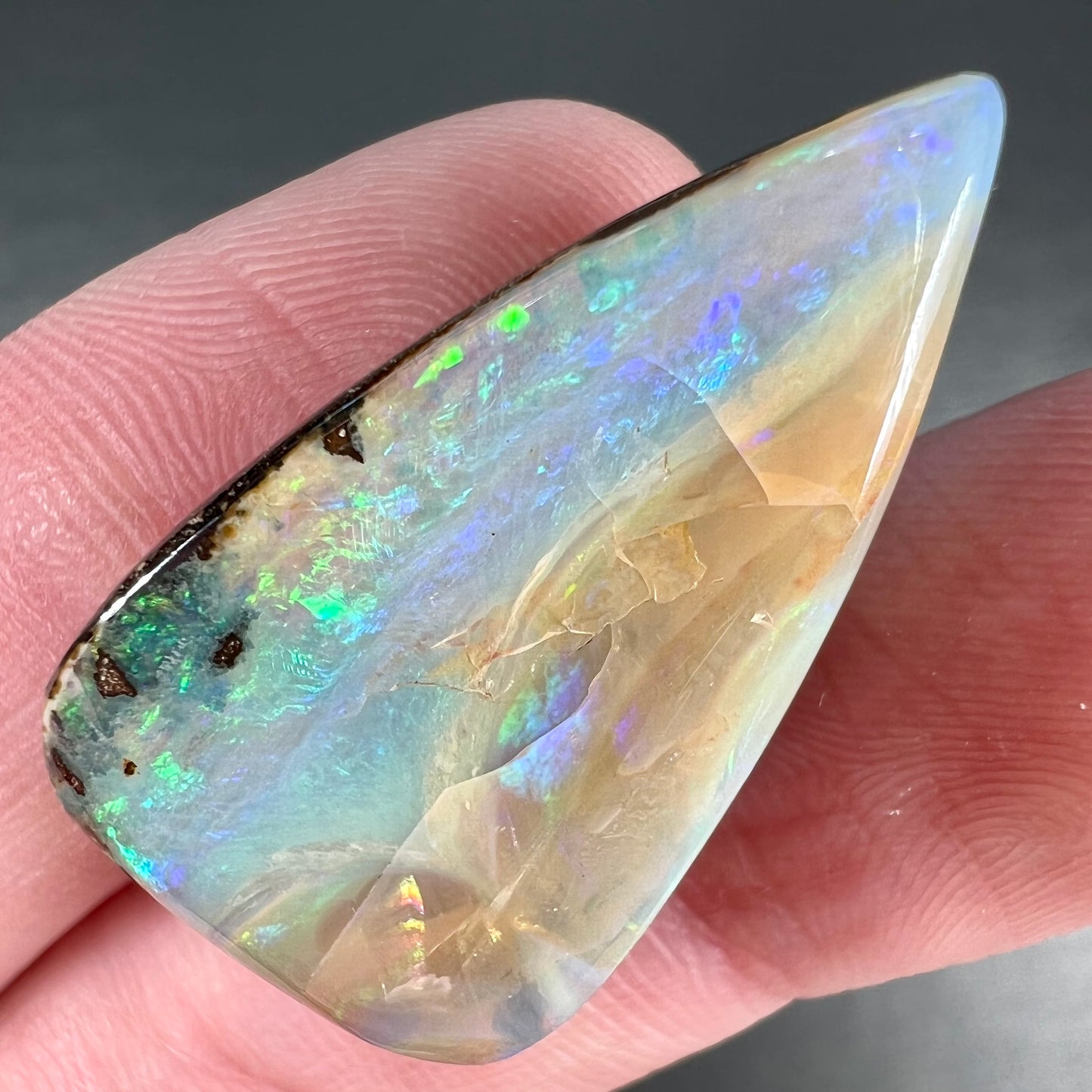 A loose, pear shaped boulder opal stone from Queensland, Australia. Predominant colors are blue, purple, and green.