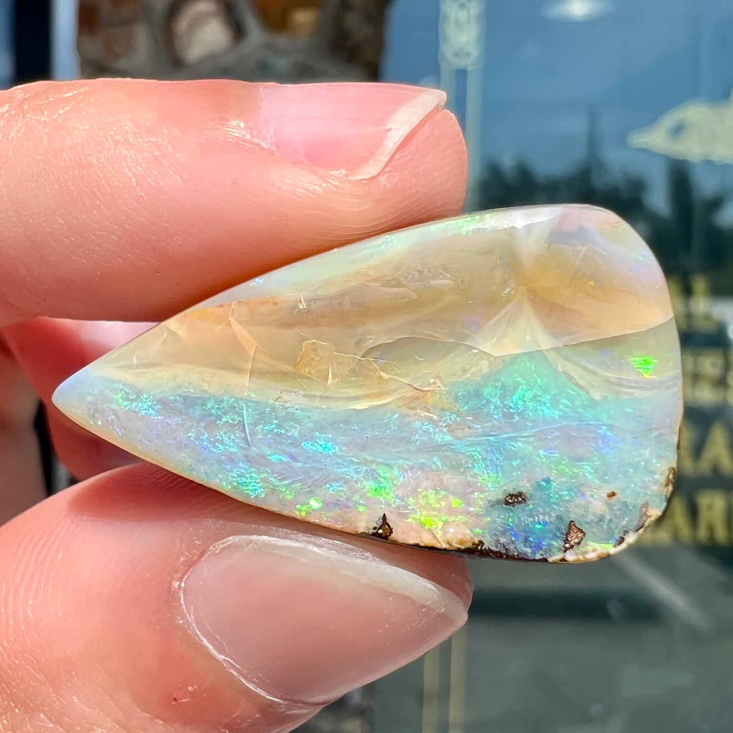 A loose, pear shaped boulder opal stone from Queensland, Australia. Predominant colors are blue, purple, and green.
