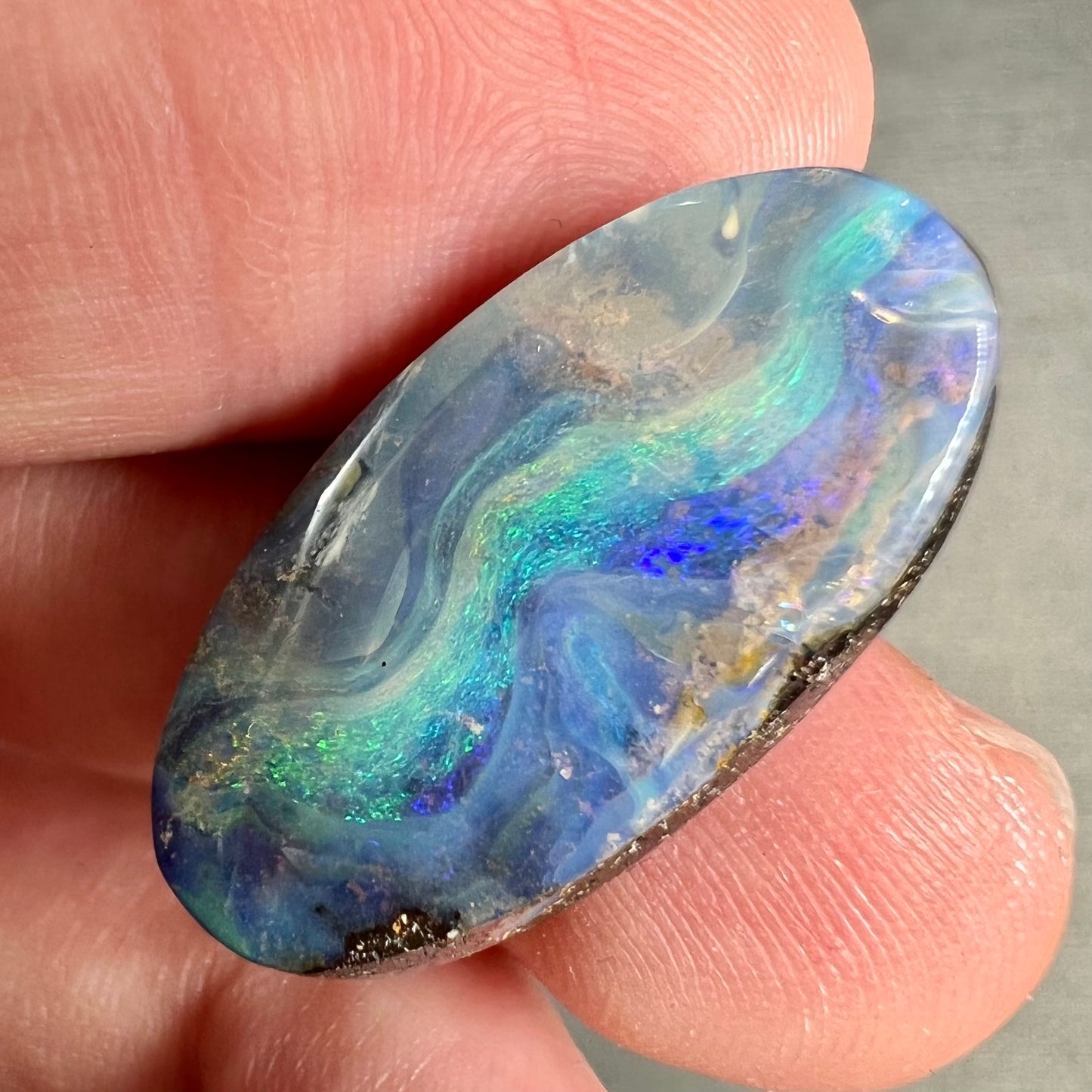 A loose, oval cabochon cut Quilpie boulder opal from Queensland, Australia. The stone is blue with green fire.