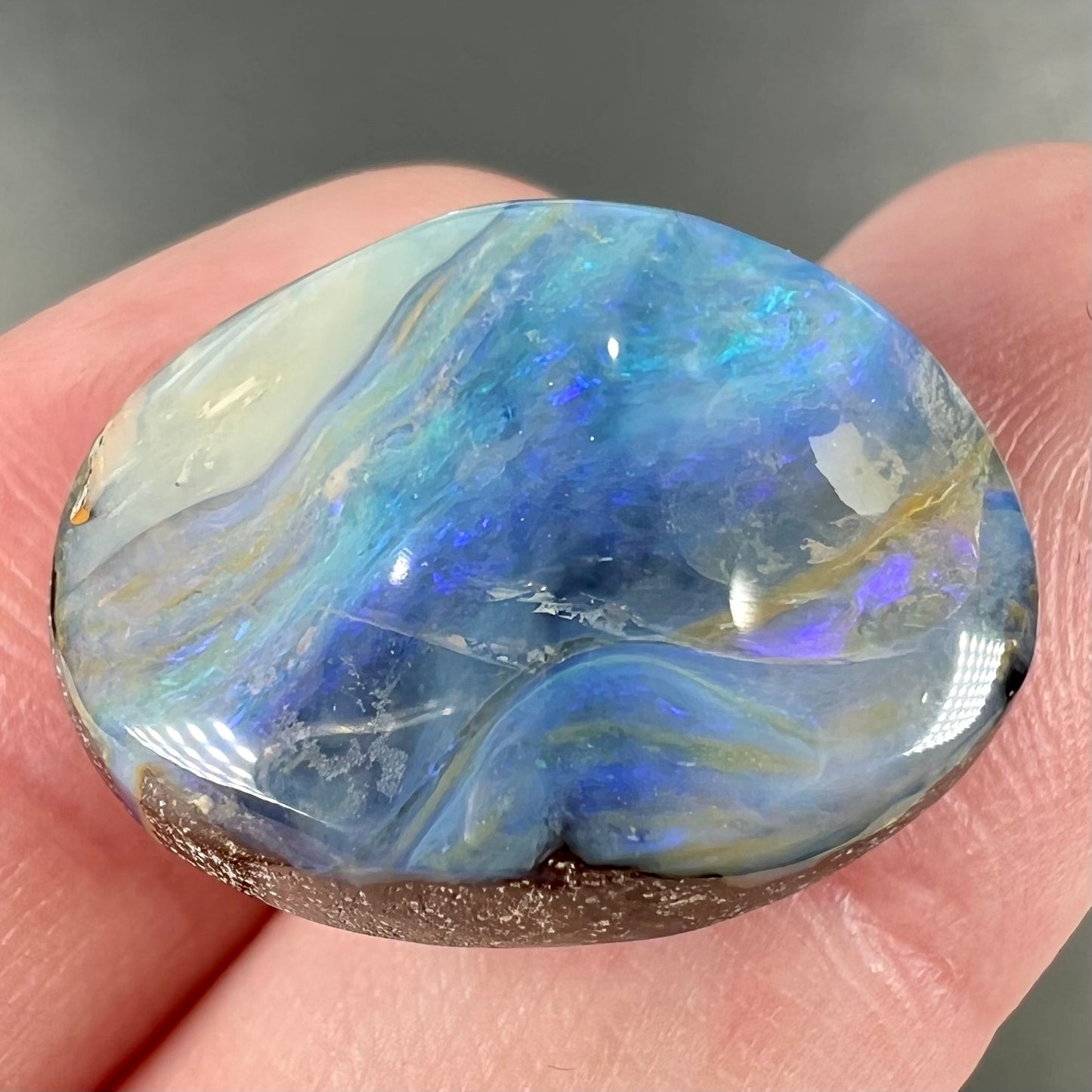 A loose, oval cabochon cut Australian boulder opal stone.