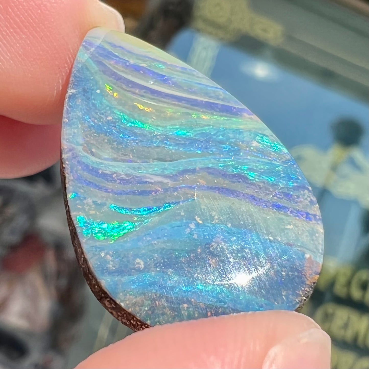 A loose, pear shaped boulder opal stone from Quilpie, Australia. The stone is predominantly blue, green, and purple with red and orange undertones.