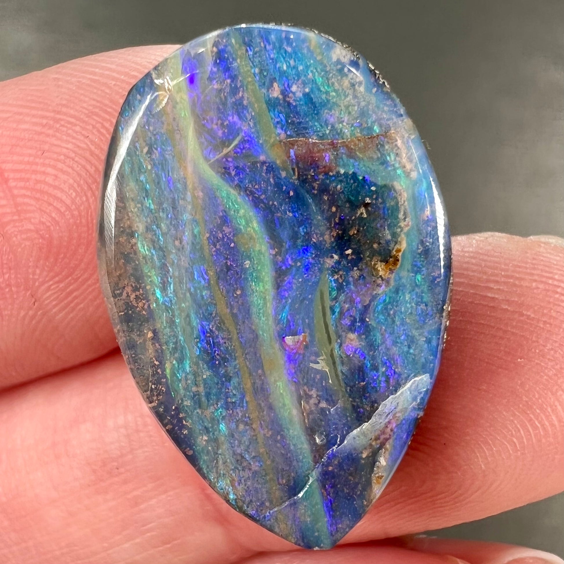 A loose, pear shaped Australian boulder opal stone.  The predominant colors are purple, green, and aqua.