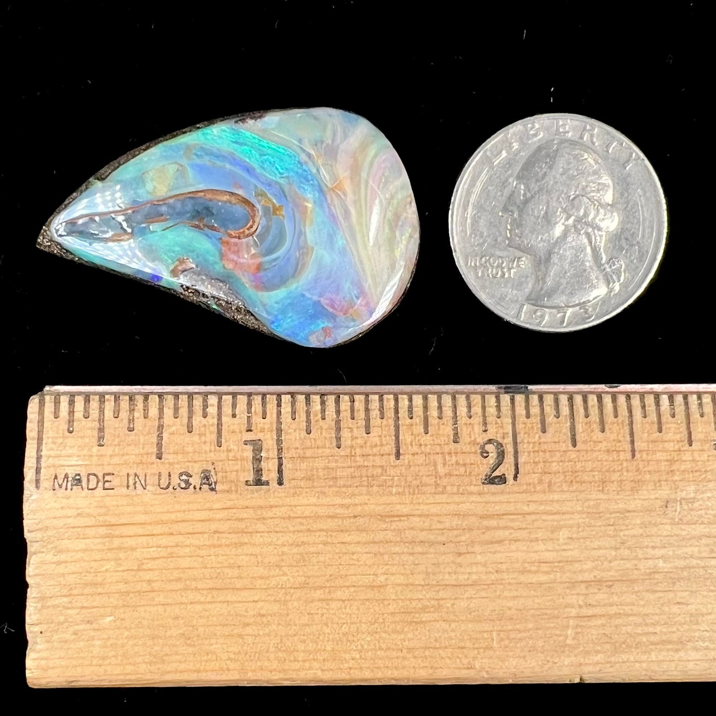 A polished pear shaped boulder opal stone from Quilpie, Australia. Predominant colors are blue, green, and aqua.