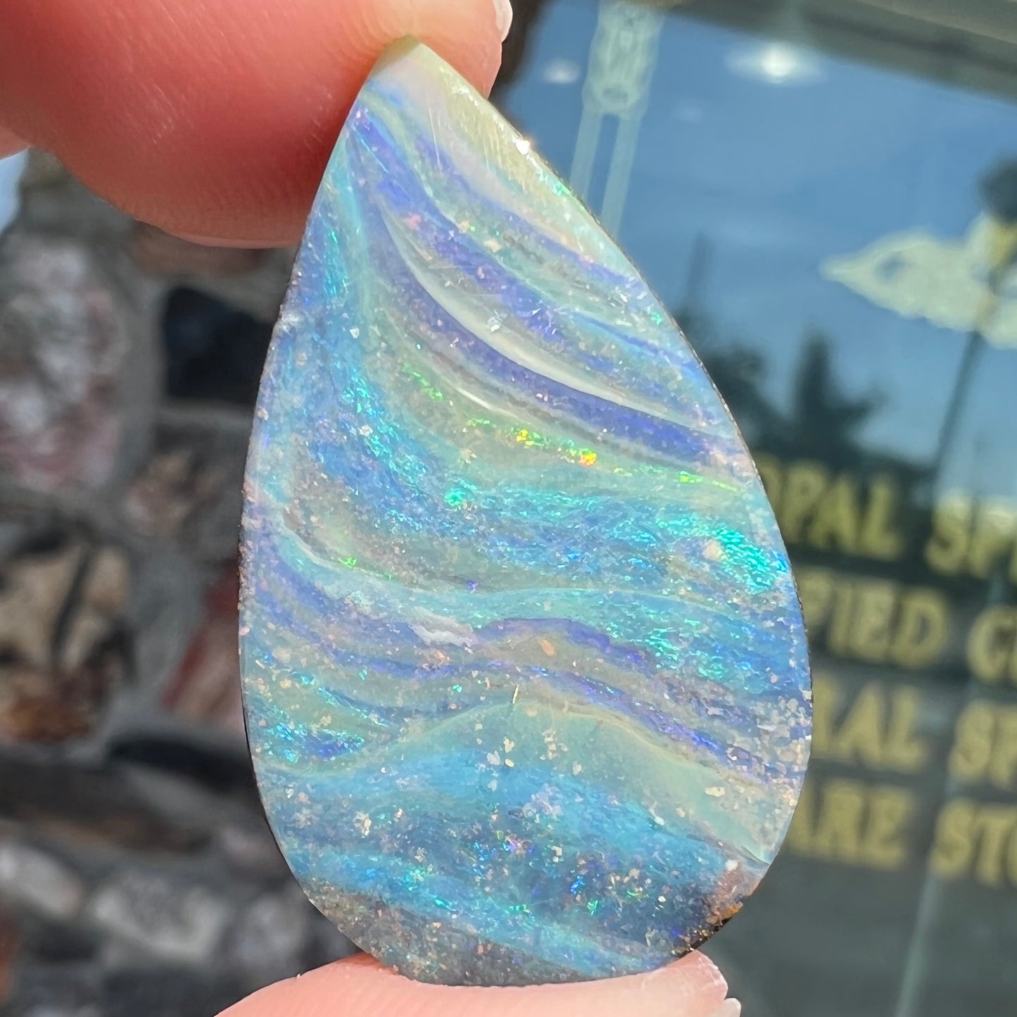 A loose, pear shaped boulder opal stone from Quilpie, Australia. The stone is predominantly blue, green, and purple with red and orange undertones.