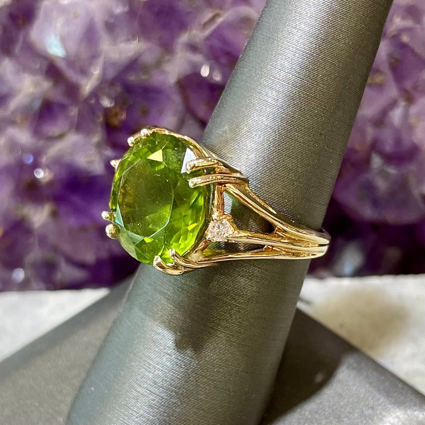 A ladies' round brilliant cut peridot statement ring set with two round diamond accents in yellow gold.