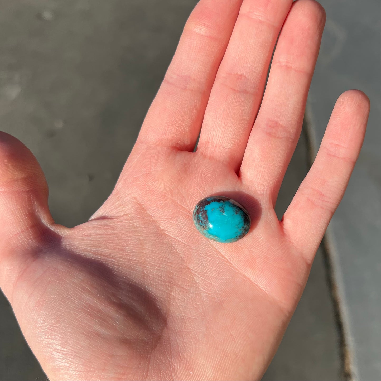 An oval cabochon cut blue turquoise stone with red cuprite inclusions from Royston District, Nevada.
