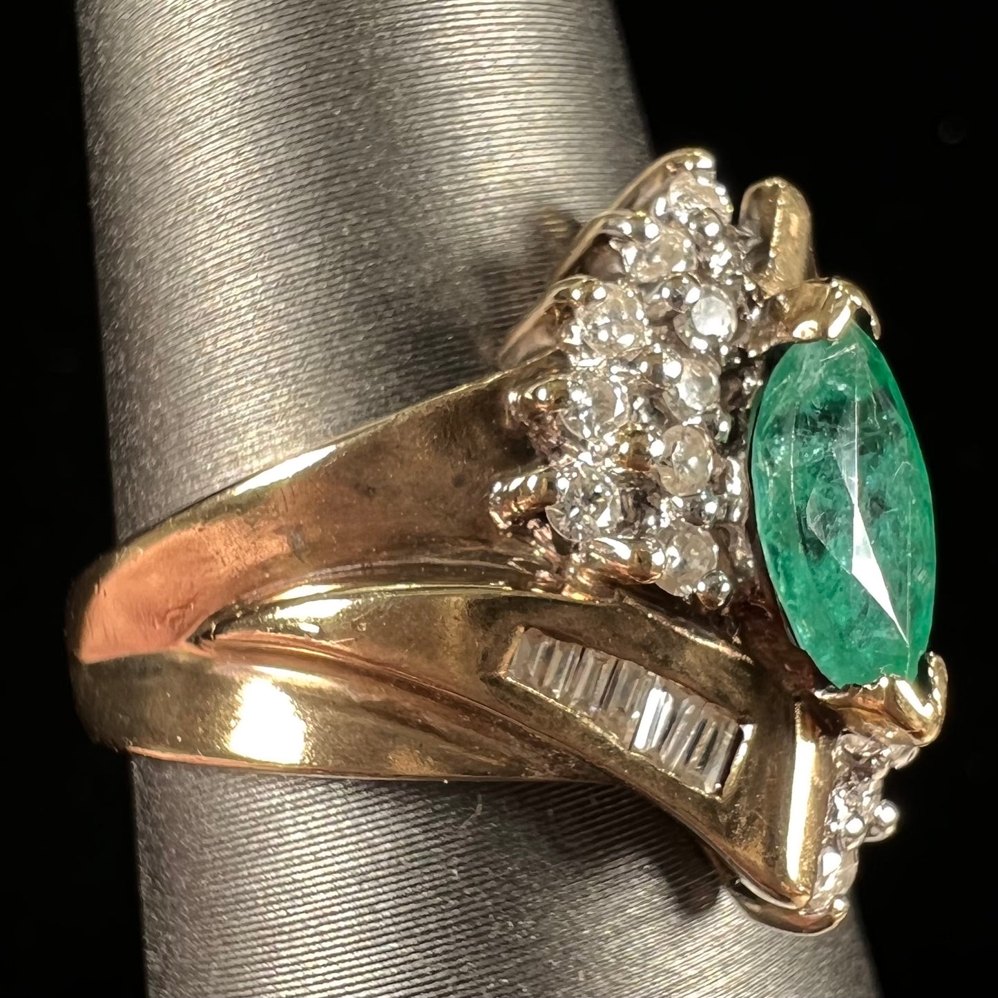 A yellow gold marquise cut emerald and diamond ring. The diamonds are prong set round cuts and channel set baguette cuts.