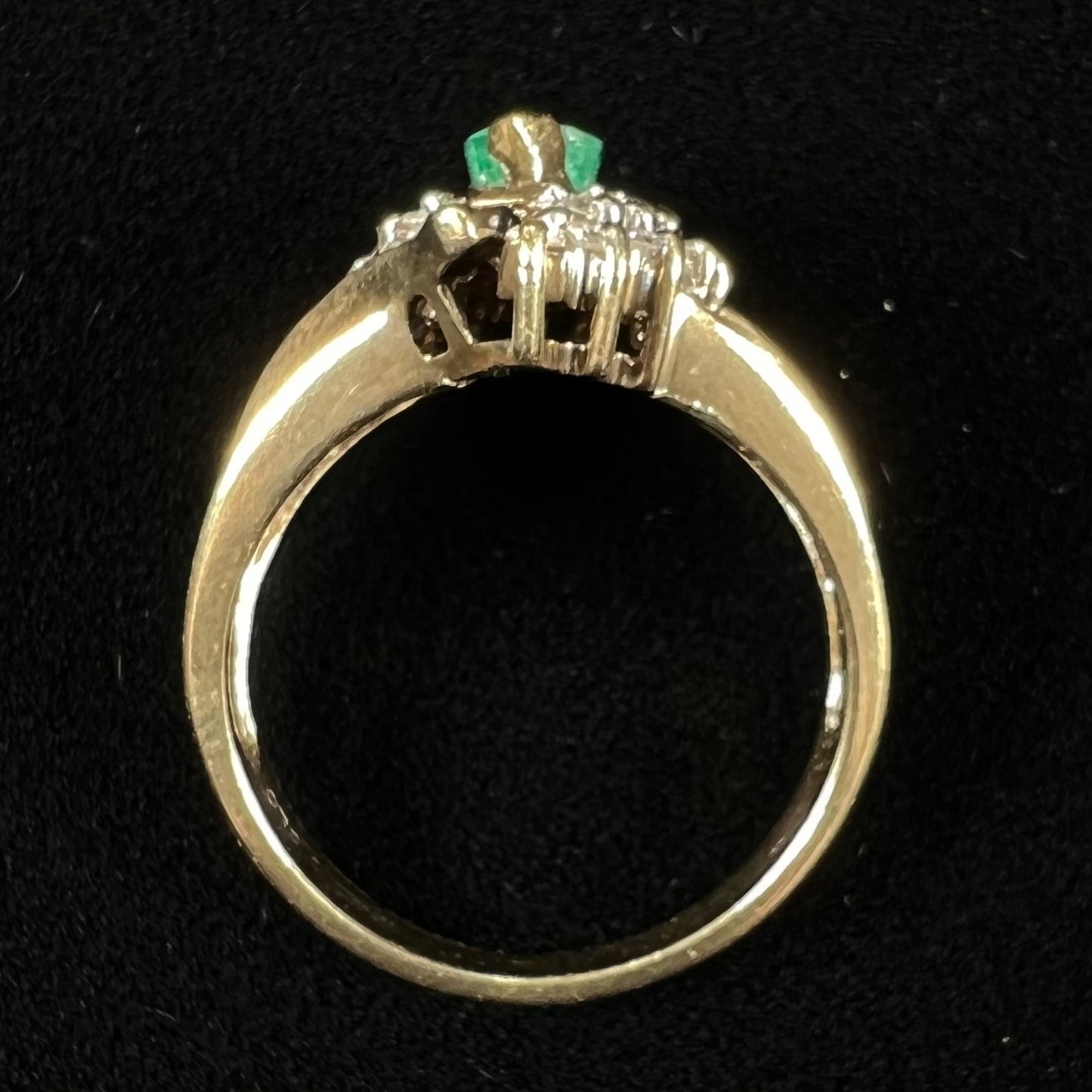 A yellow gold marquise cut emerald and diamond ring. The diamonds are prong set round cuts and channel set baguette cuts.