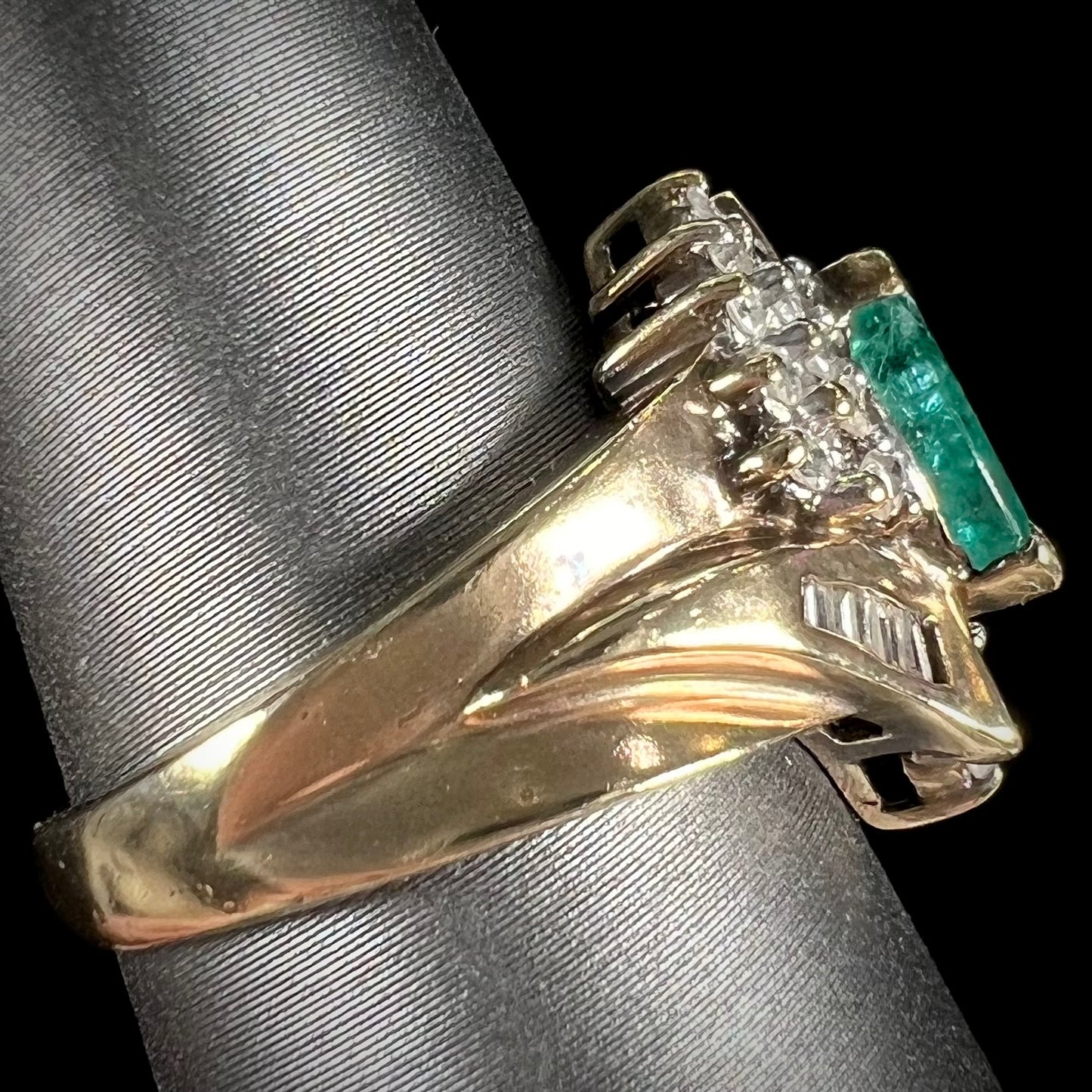 A yellow gold marquise cut emerald and diamond ring. The diamonds are prong set round cuts and channel set baguette cuts.