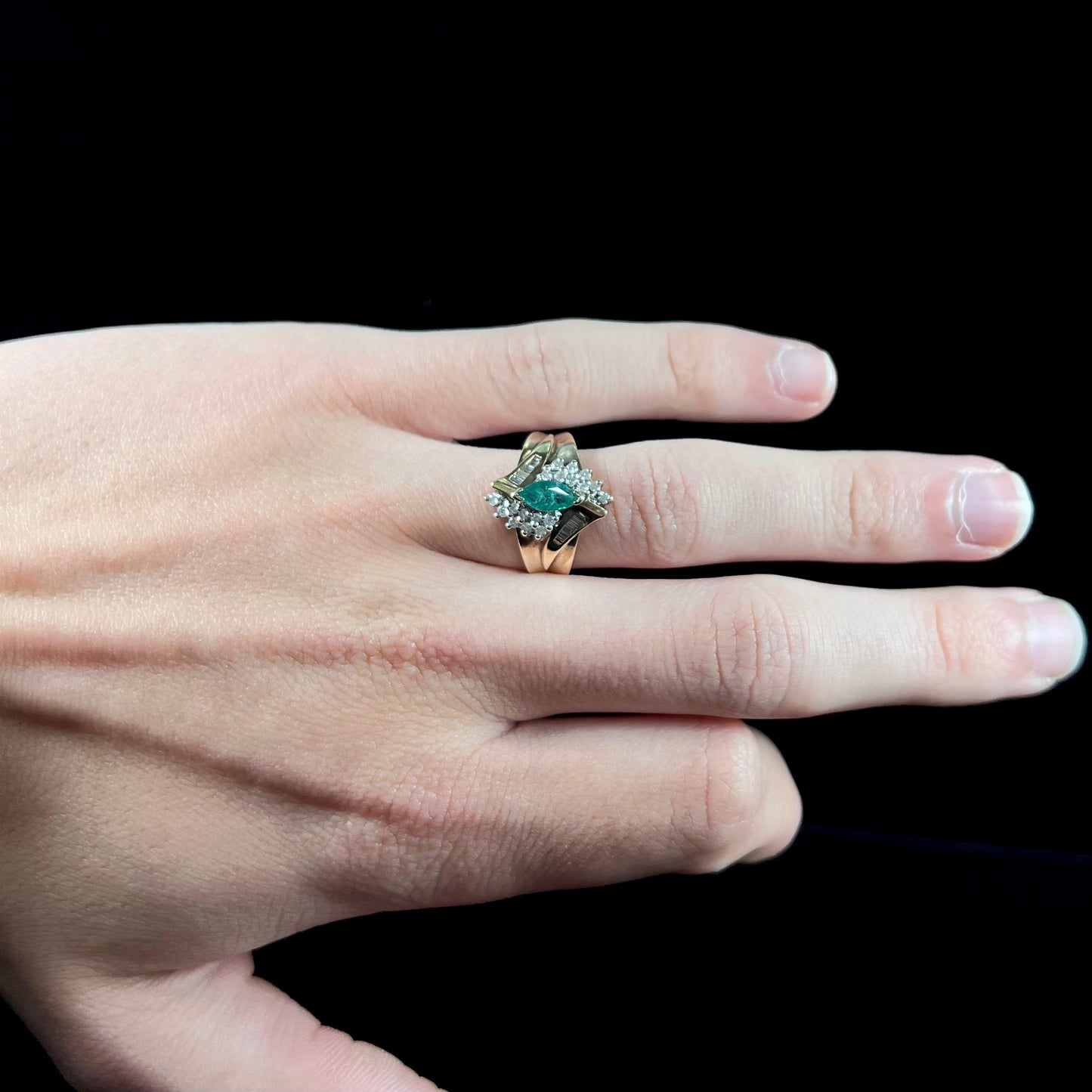 A yellow gold marquise cut emerald and diamond ring. The diamonds are prong set round cuts and channel set baguette cuts.