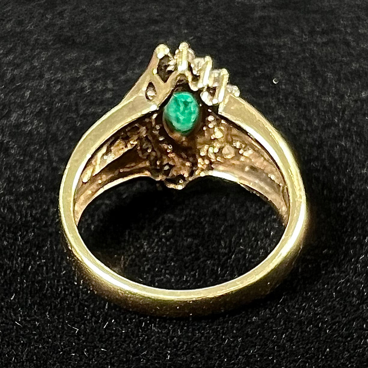 A yellow gold marquise cut emerald and diamond ring. The diamonds are prong set round cuts and channel set baguette cuts.