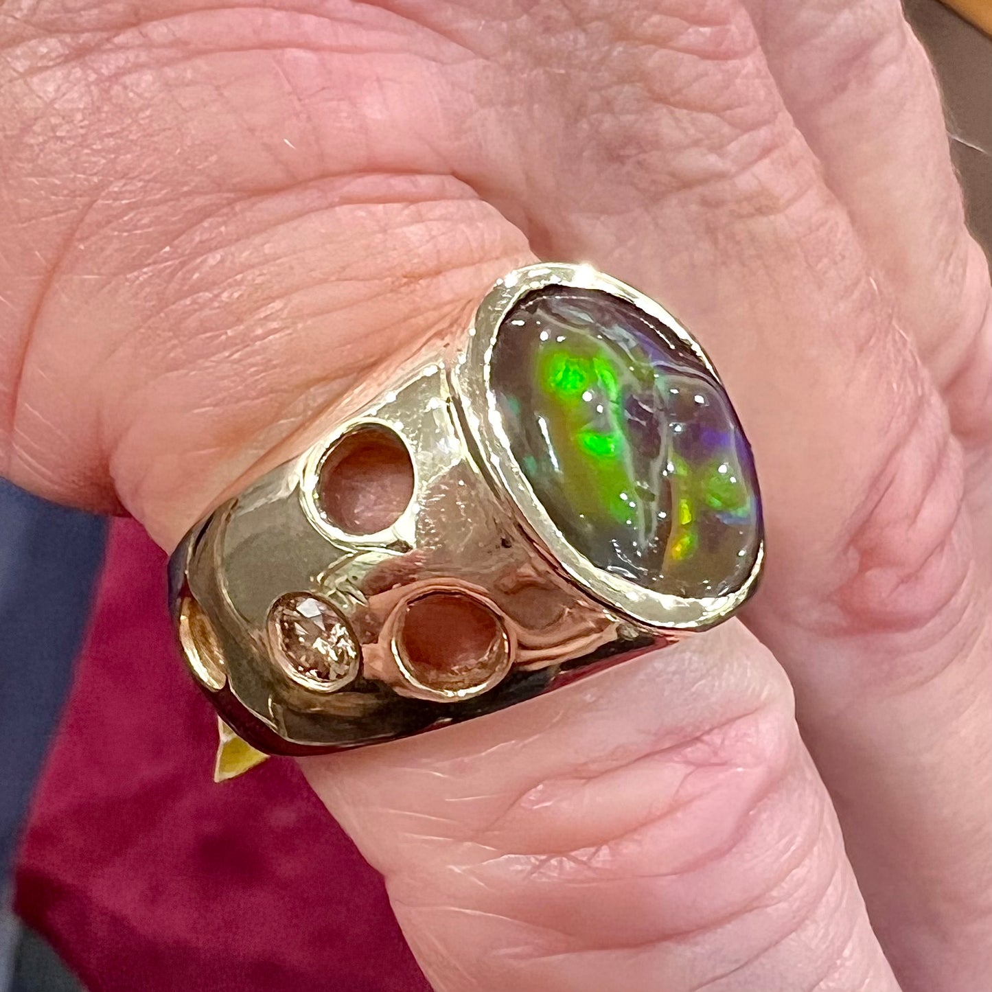 Men's rainbow fire agate ring set in yellow gold with champagne diamonds. The ring style has holes.