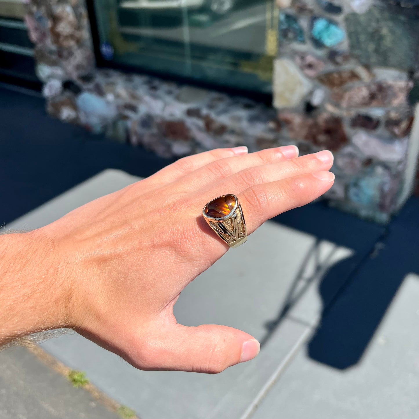 A solid, yellow gold men's fire agate ring. The predominant color is red with green undertones.