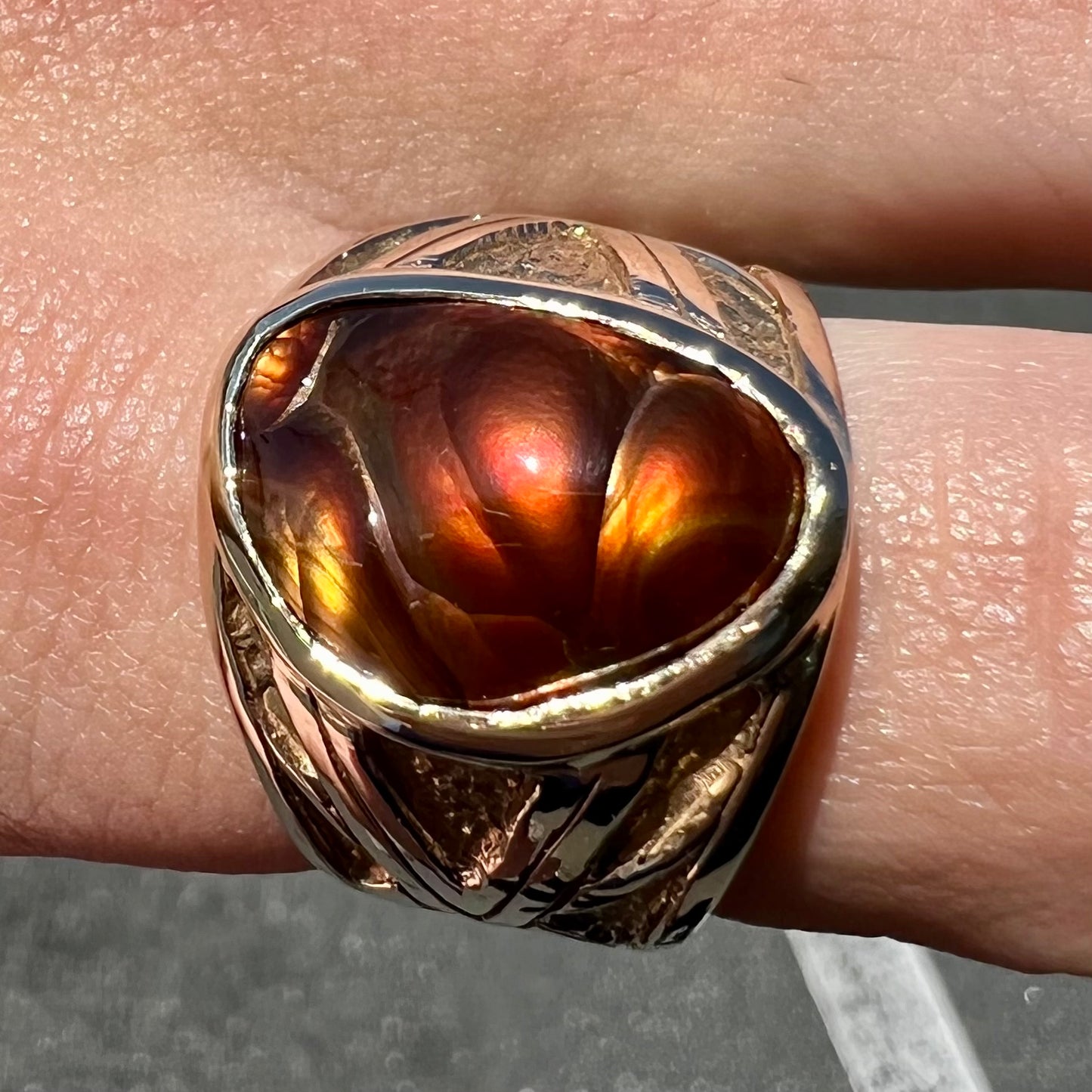 A solid, yellow gold men's fire agate ring. The predominant color is red with green undertones.