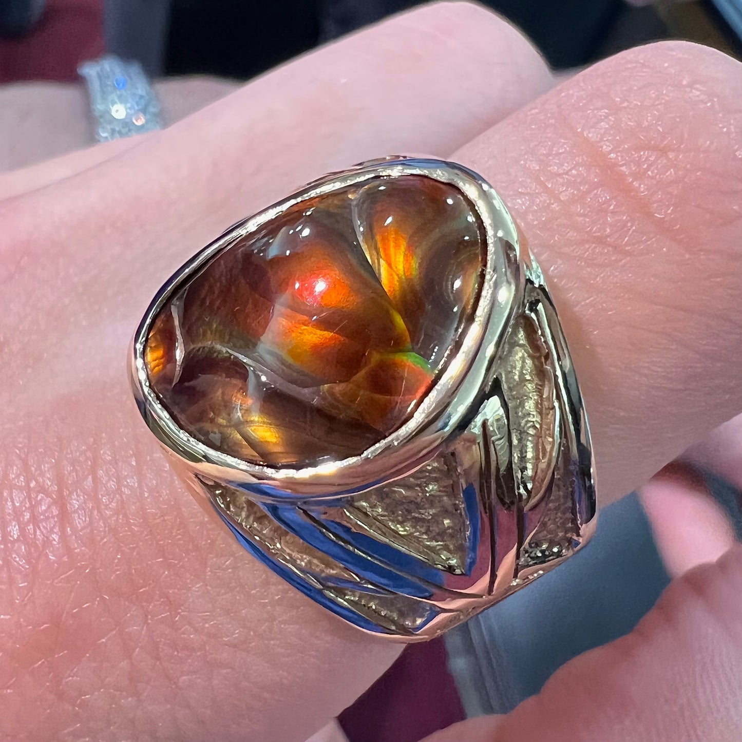 A solid, yellow gold men's fire agate ring. The predominant color is red with green undertones.