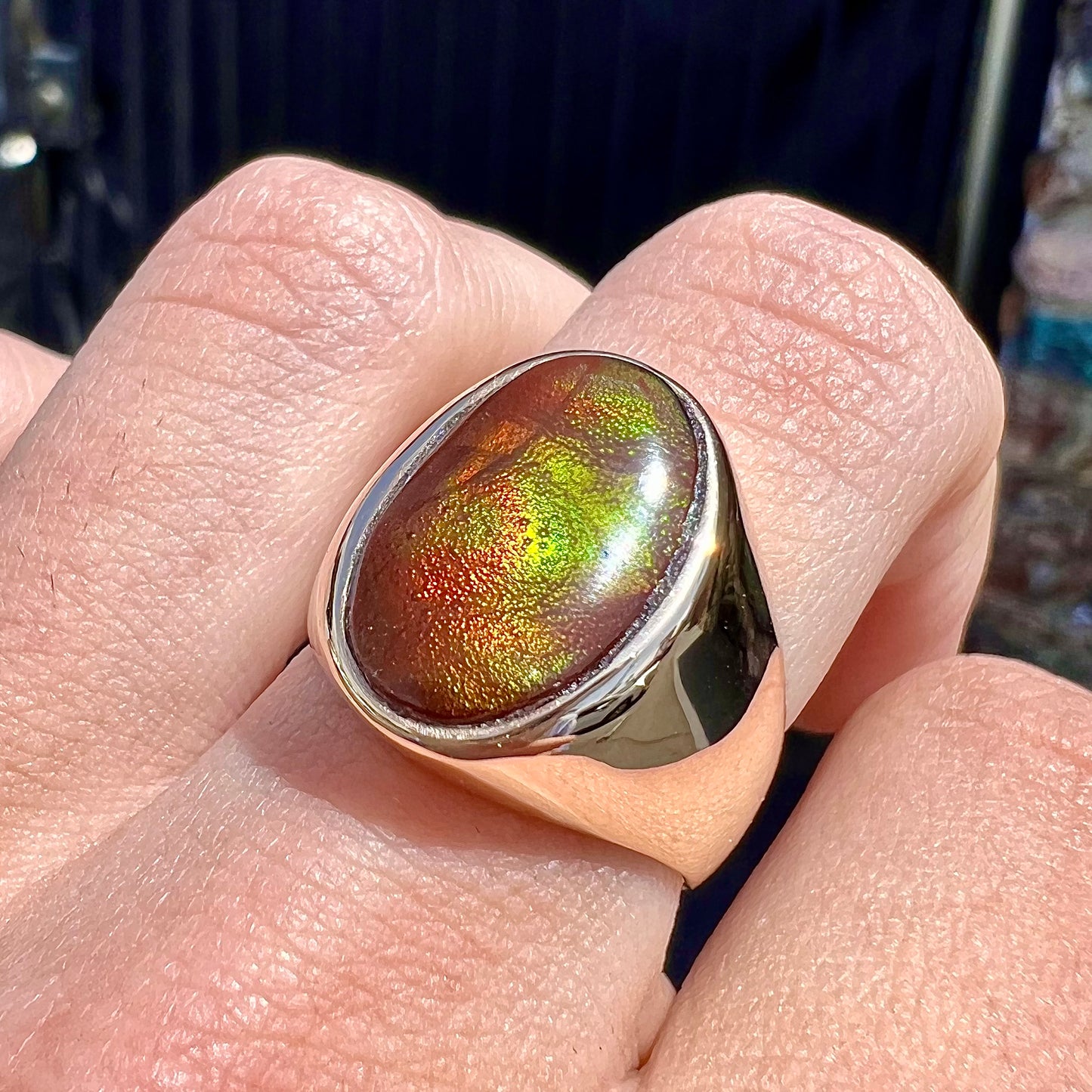 A yellow gold solitaire fire agate men's ring. The fire agate is oval shape, and red and green in color.
