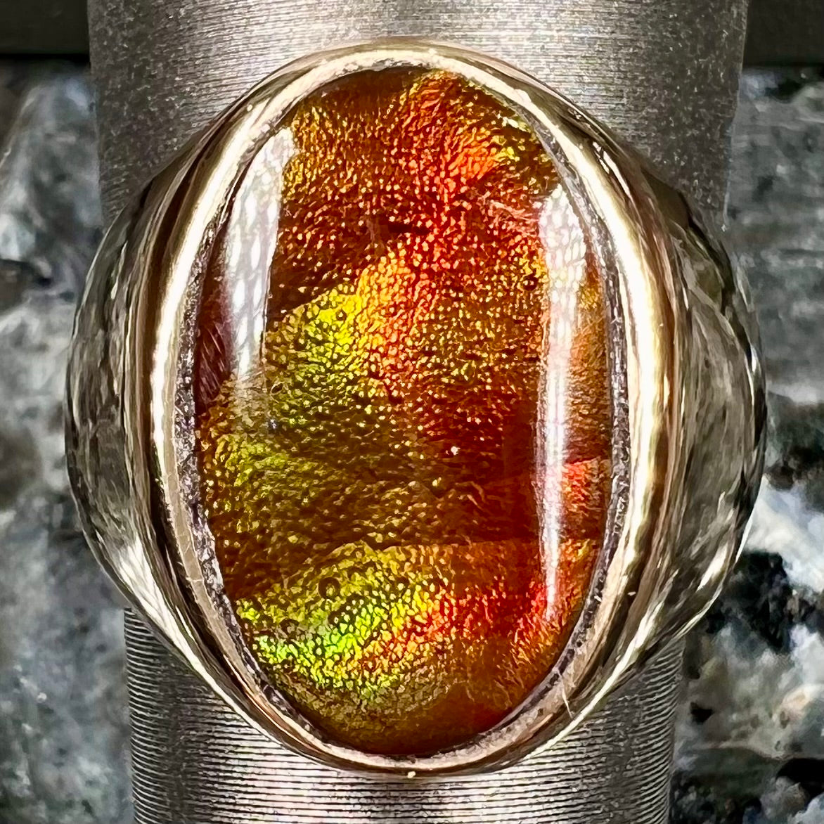 A yellow gold solitaire fire agate men's ring. The fire agate is oval shape, and red and green in color.