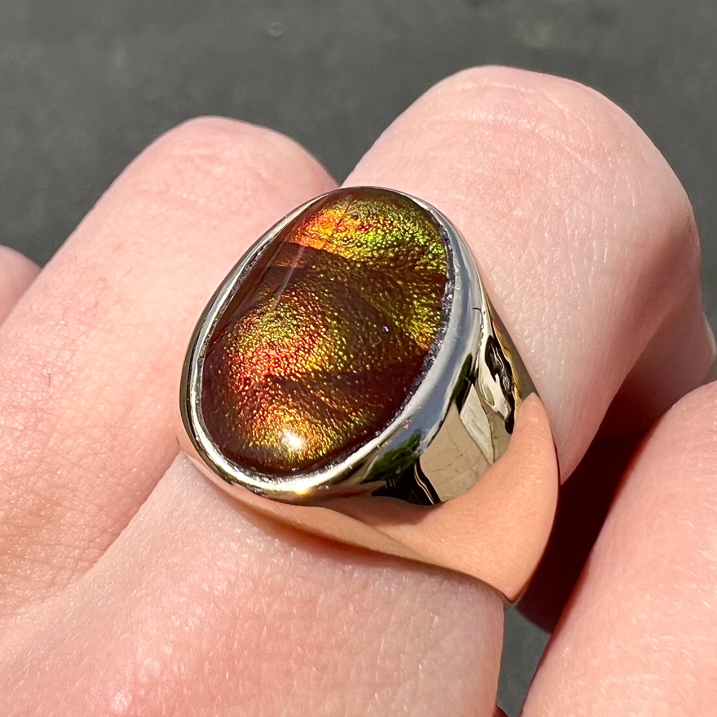 A yellow gold solitaire fire agate men's ring. The fire agate is oval shape, and red and green in color.