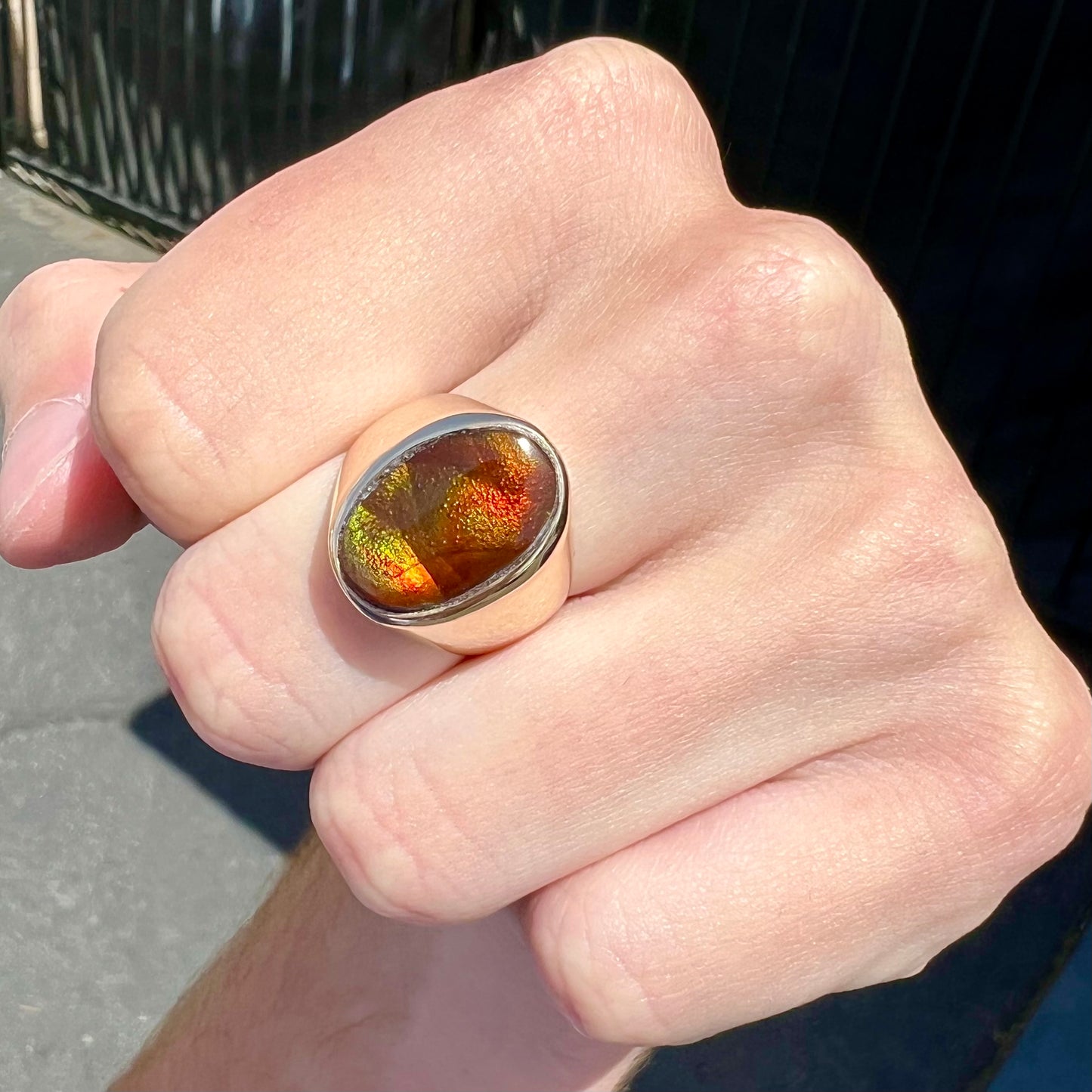 A yellow gold solitaire fire agate men's ring. The fire agate is oval shape, and red and green in color.