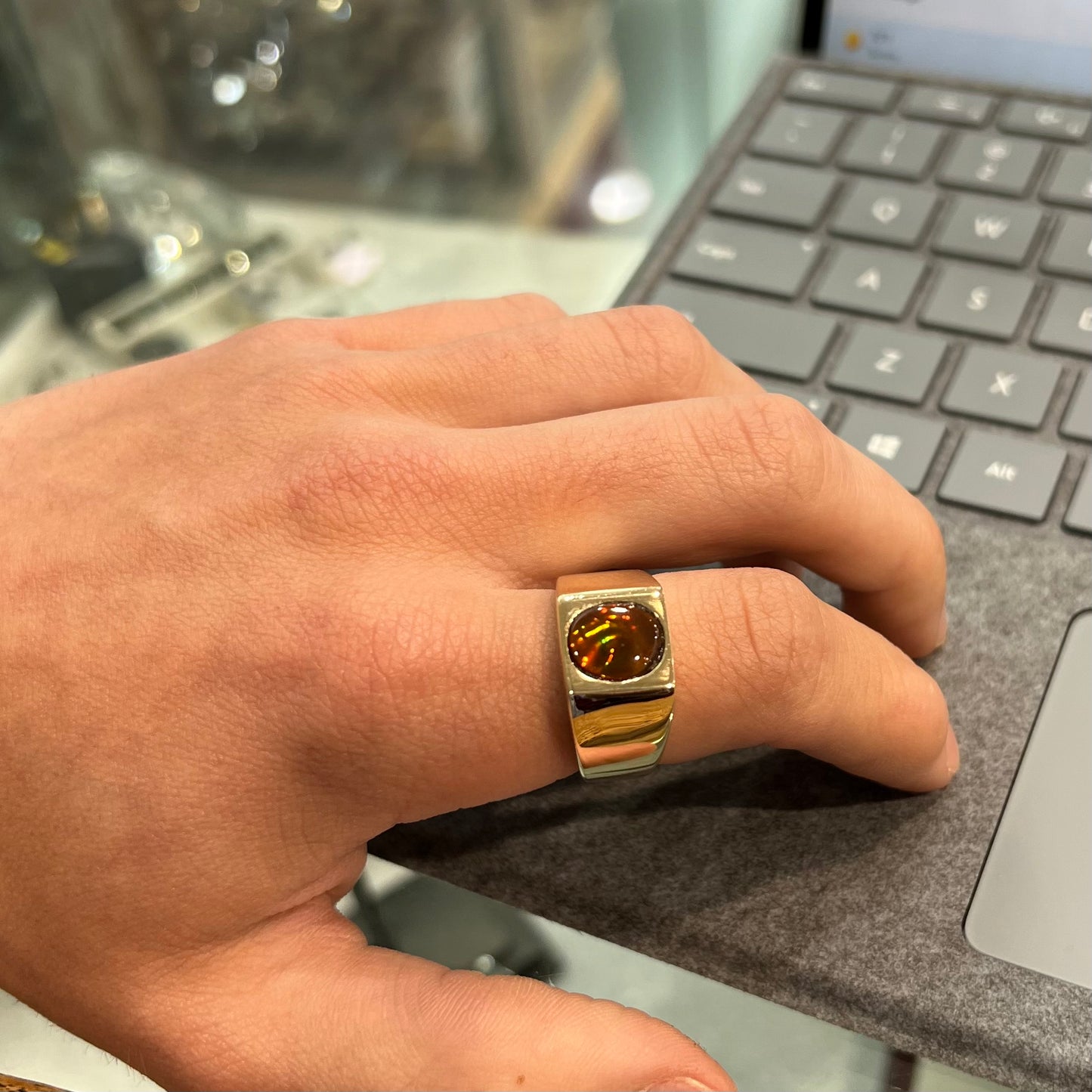 A men's yellow gold flush set fire agate solitaire ring. The fire agate displays flashes of green, orange, and yellow.