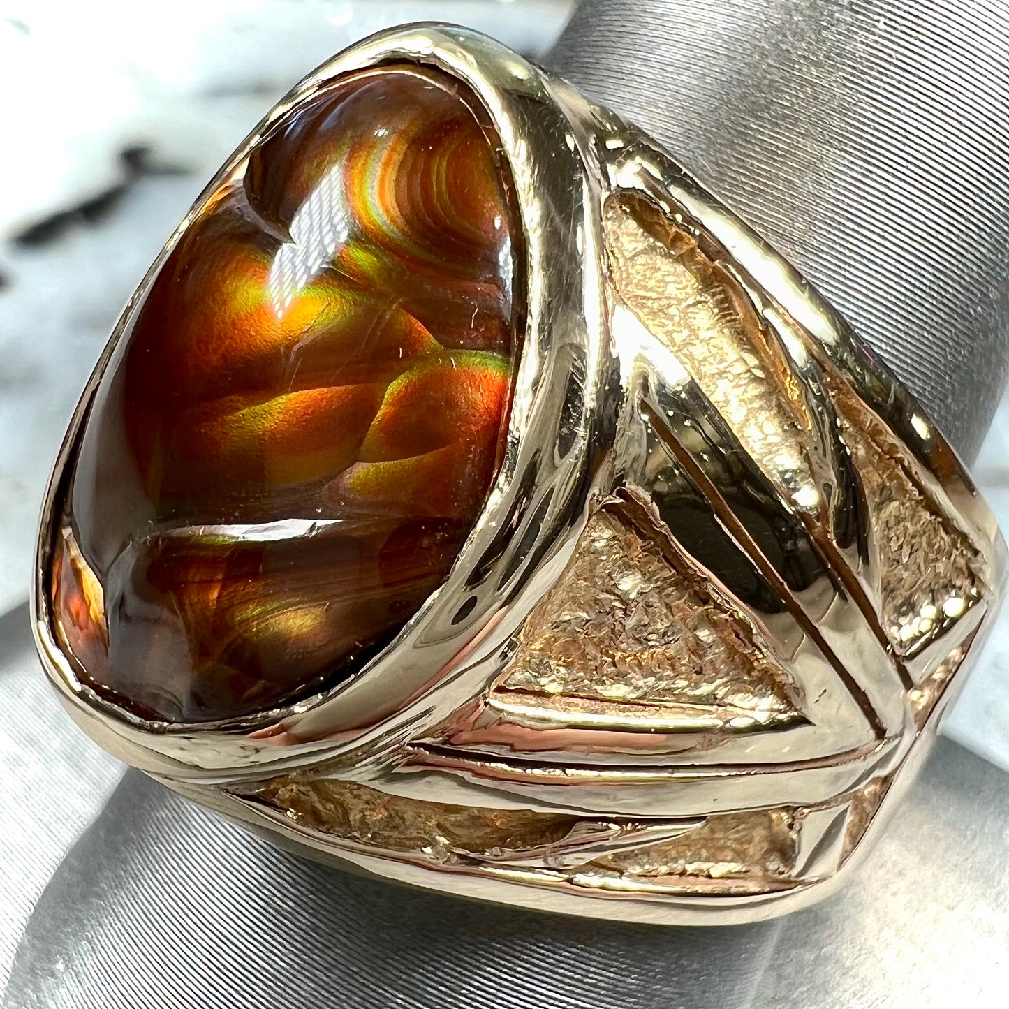 A solid, yellow gold men's fire agate ring. The predominant color is red with green undertones.