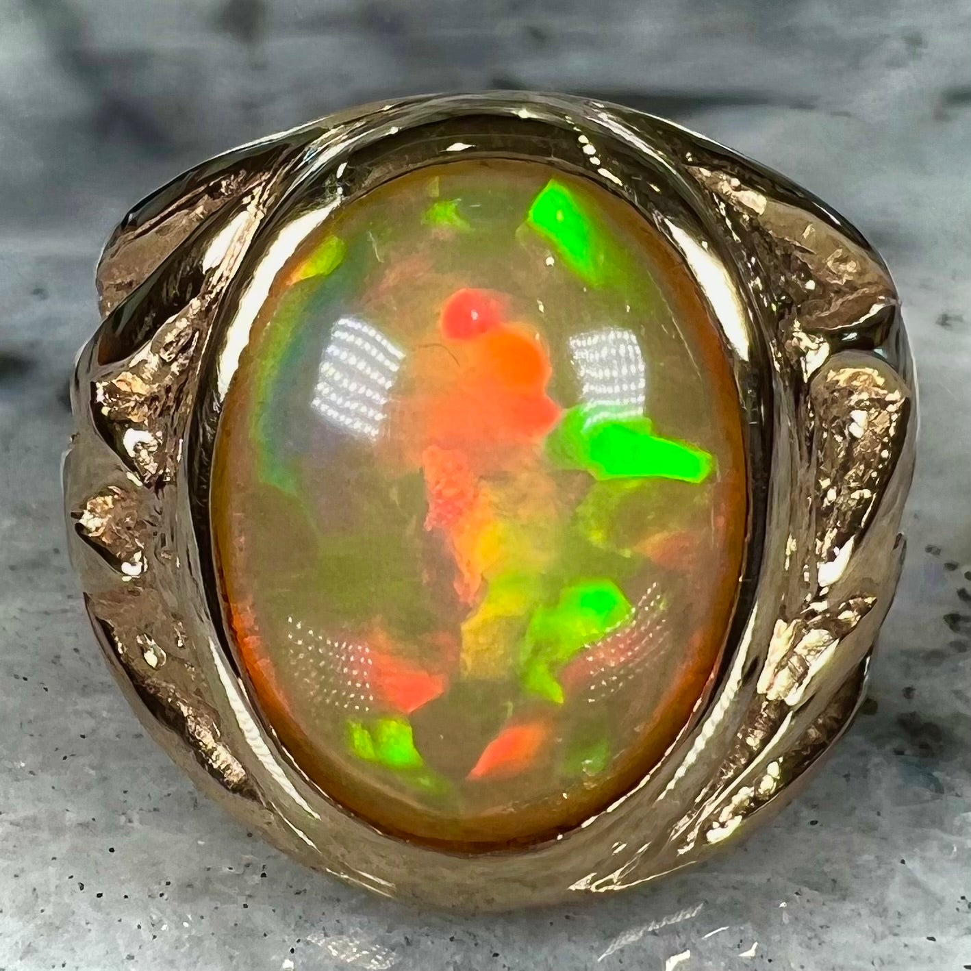 A solid yellow gold solitaire men's fire opal ring. The stone is an orange oval cabochon cut.