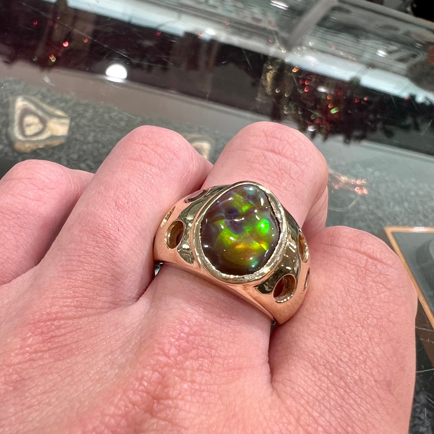 Men's rainbow fire agate ring set in yellow gold with champagne diamonds. The ring style has holes.