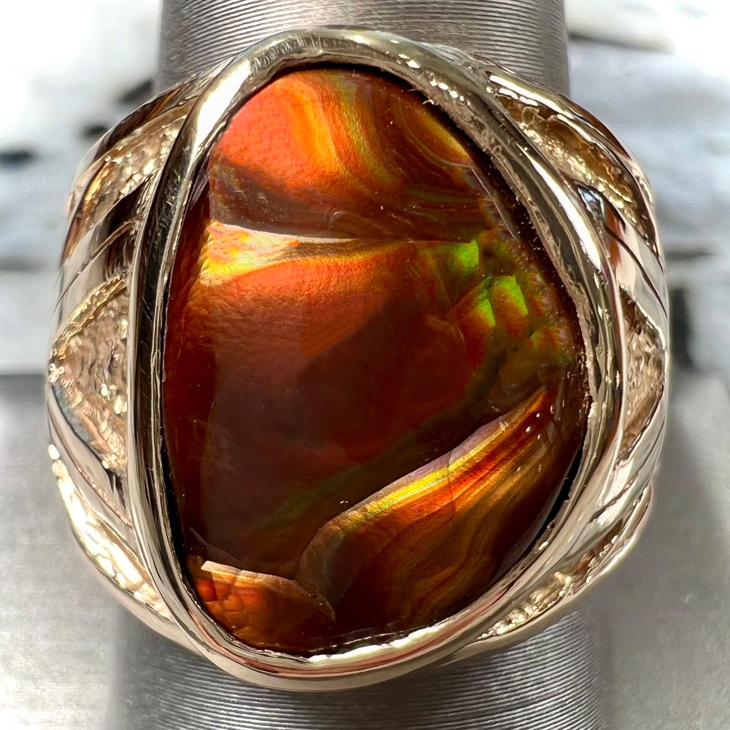 A solid, yellow gold men's fire agate ring. The predominant color is red with green undertones.