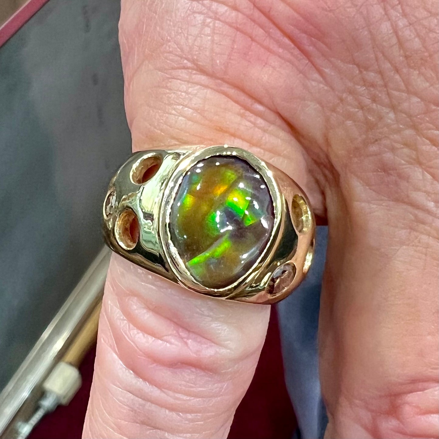 Men's rainbow fire agate ring set in yellow gold with champagne diamonds. The ring style has holes.