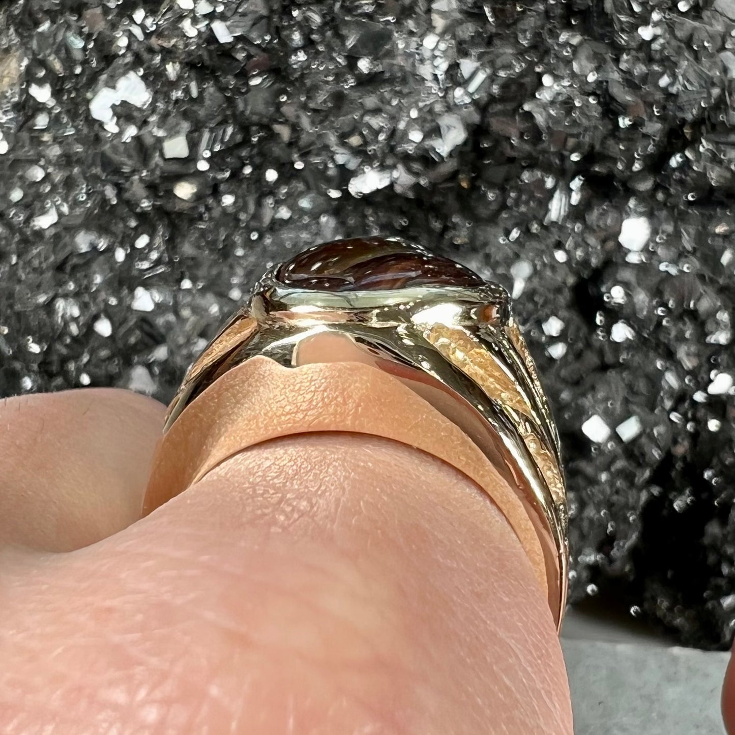 A solid, yellow gold men's fire agate ring. The predominant color is red with green undertones.