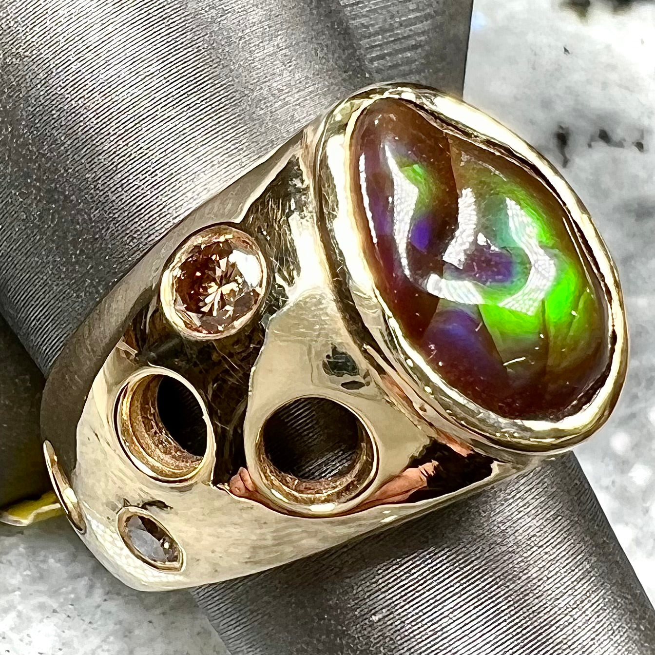 Men's rainbow fire agate ring set in yellow gold with champagne diamonds. The ring style has holes.