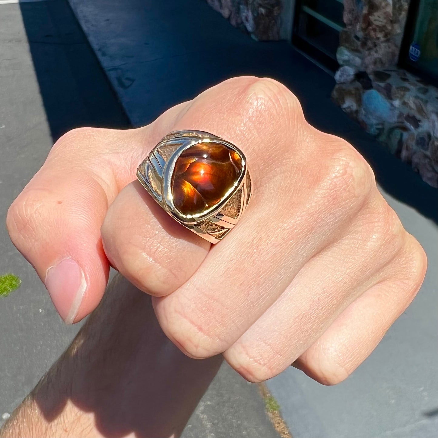 A solid, yellow gold men's fire agate ring. The predominant color is red with green undertones.