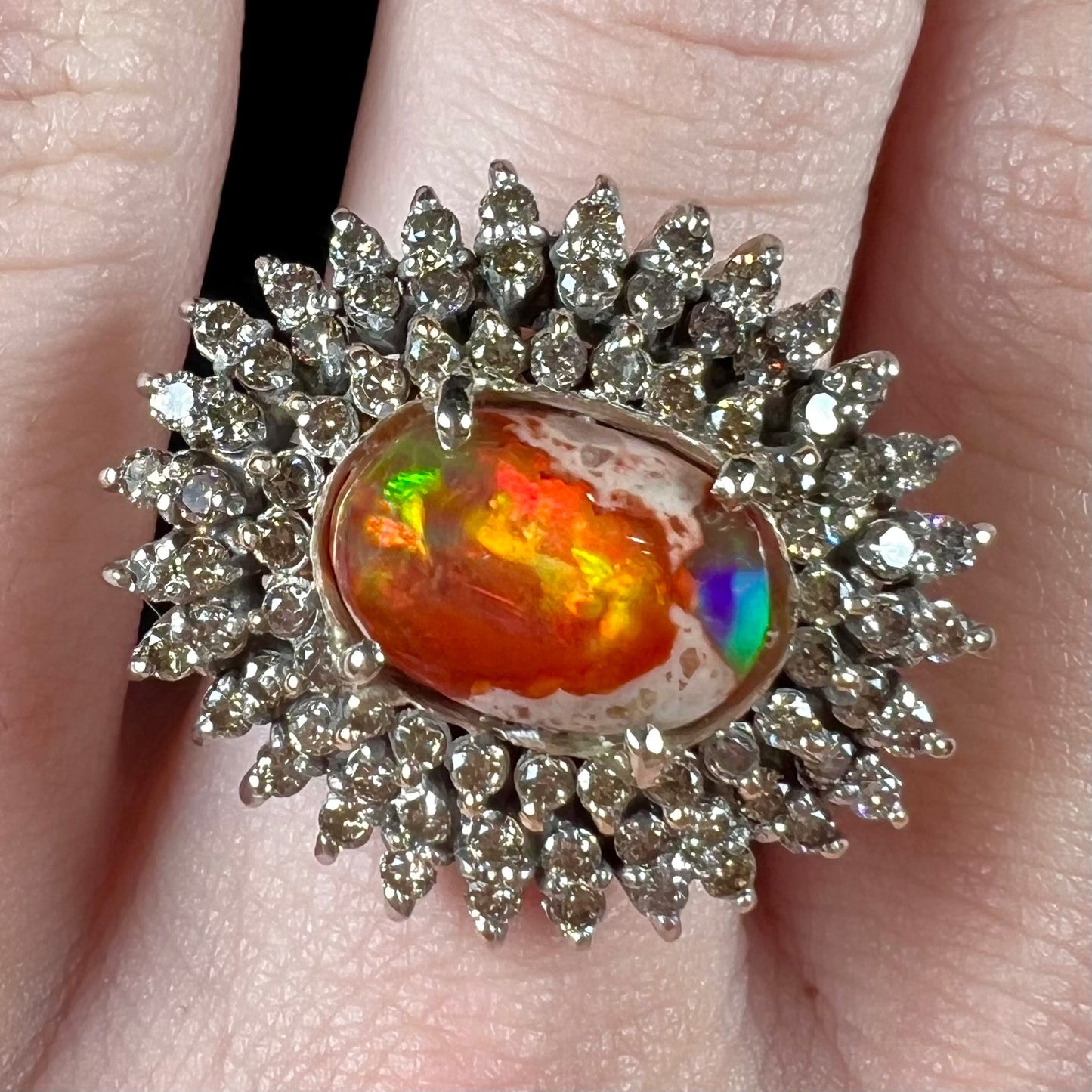 An 18k white gold orange fire opal ring set with a triple halo of diamonds.