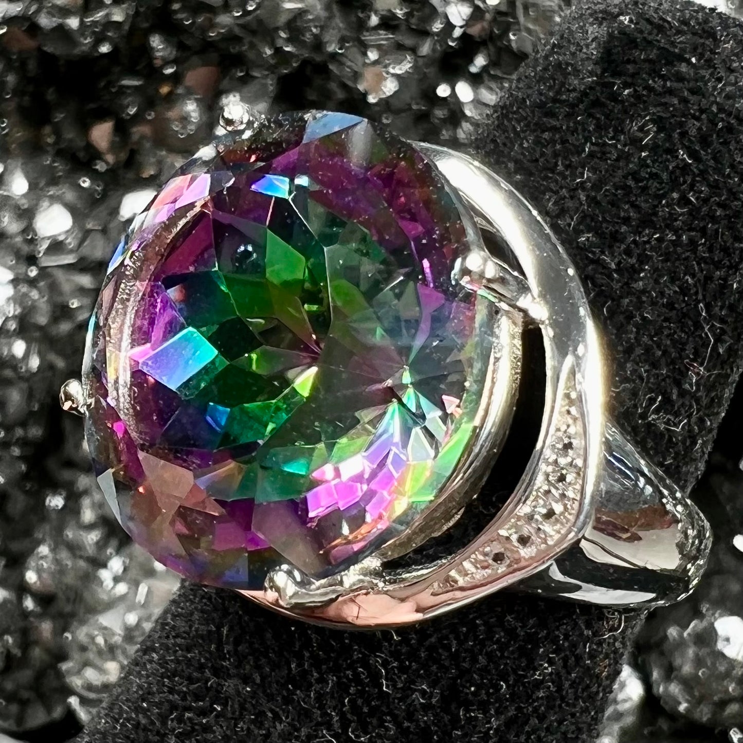 A large, round cut pink and green mystic topaz set in a sterling silver ring with white topaz accent stones.