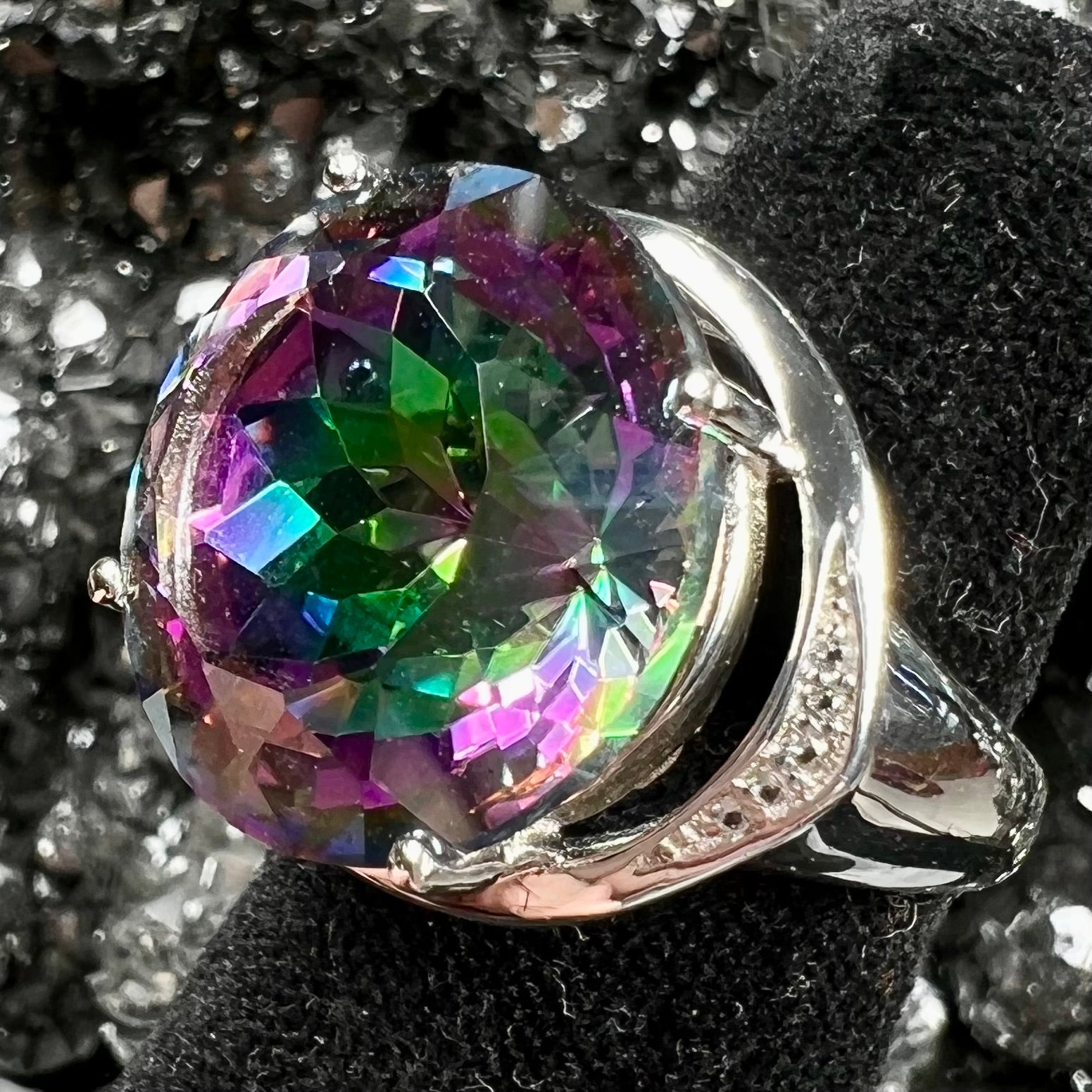 A large, round cut pink and green mystic topaz set in a sterling silver ring with white topaz accent stones.
