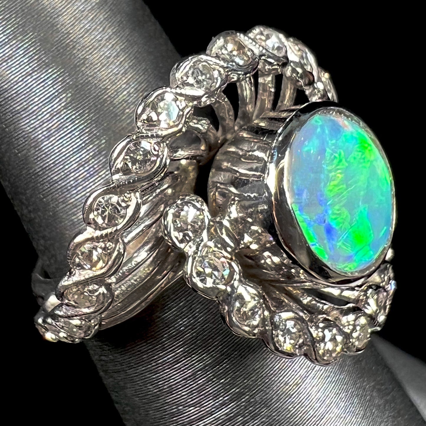 A white gold ring featuring a round cabochon cut black opal set in a swirl of round cut diamonds.