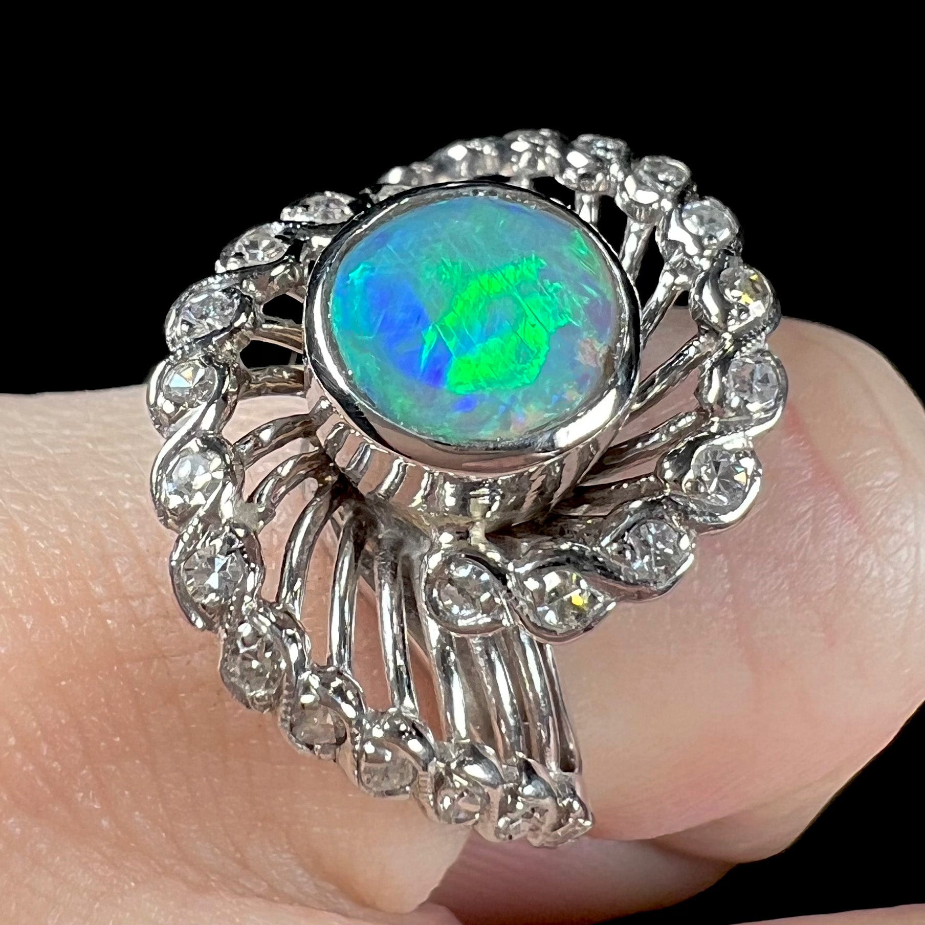 A white gold ring featuring a round cabochon cut black opal set in a swirl of round cut diamonds.