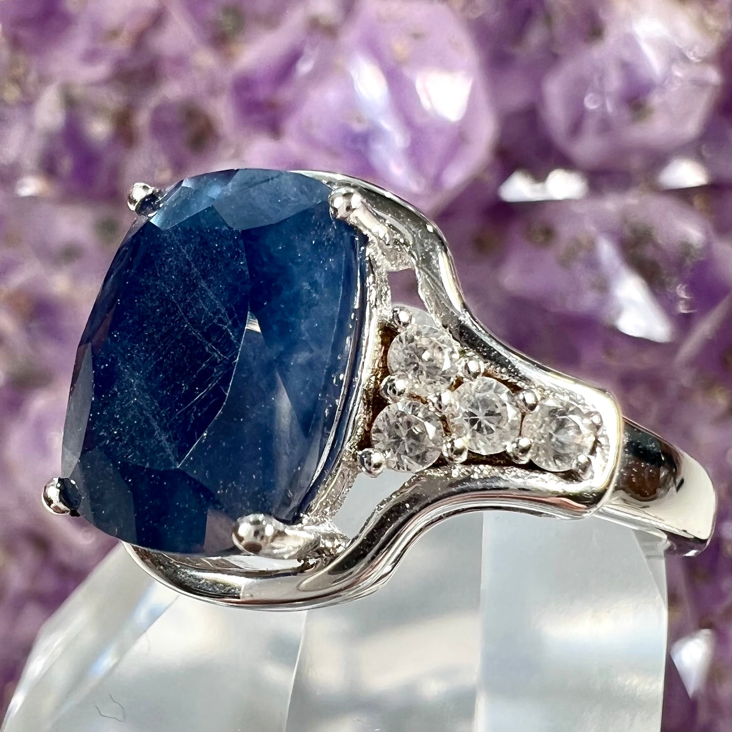 A sterling silver ring set with a cushion cut blue sapphire center stone and round cut white sapphire accents.