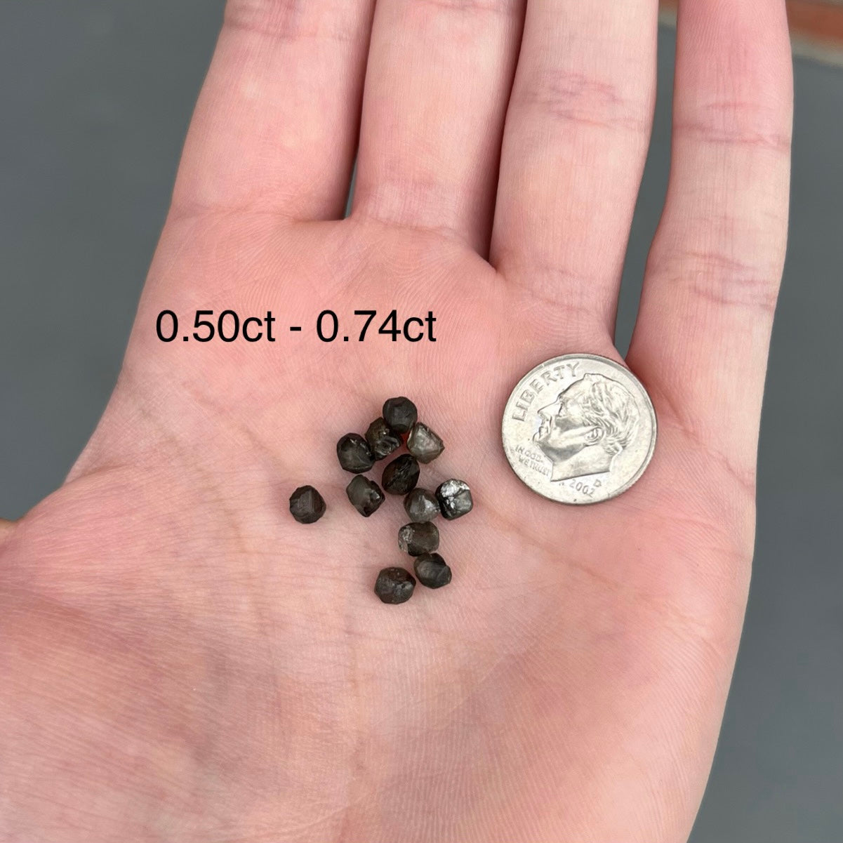 A selection of black diamond crystals ranging from half of a carat to 0.74 carat next to a dime.