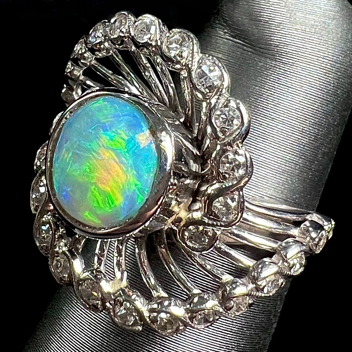 A white gold ring featuring a round cabochon cut black opal set in a swirl of round cut diamonds.