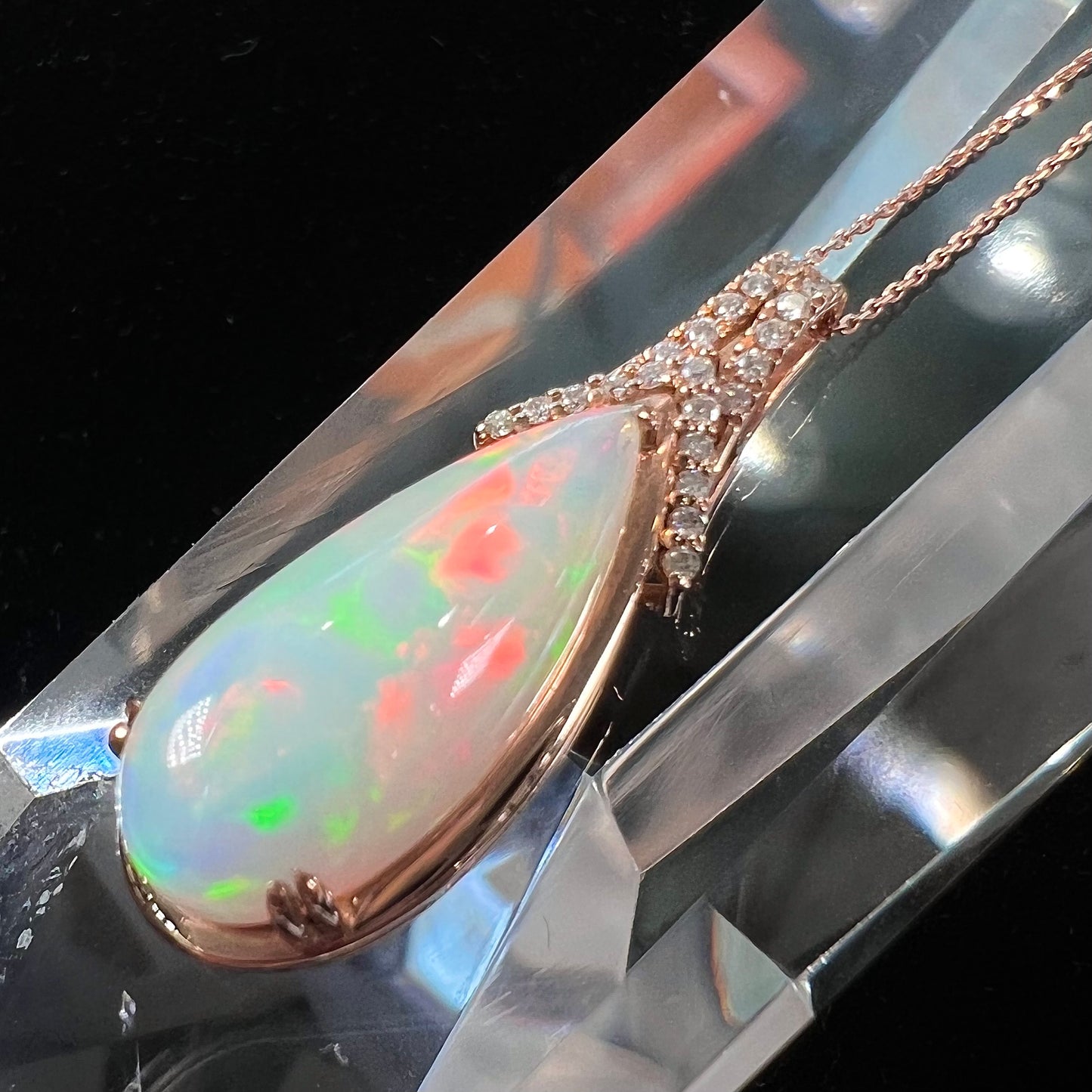 A rose gold, teardrop shaped fire opal and diamond necklace on a cable chain.