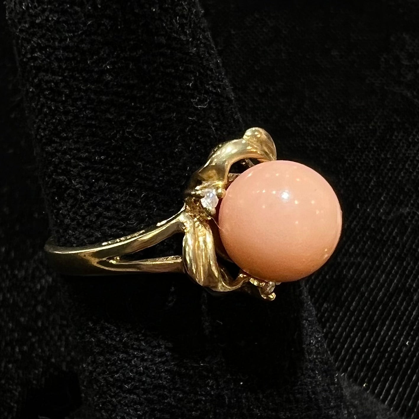 A vintage split shank flower ring set with a round pink coral sphere and diamond accents.